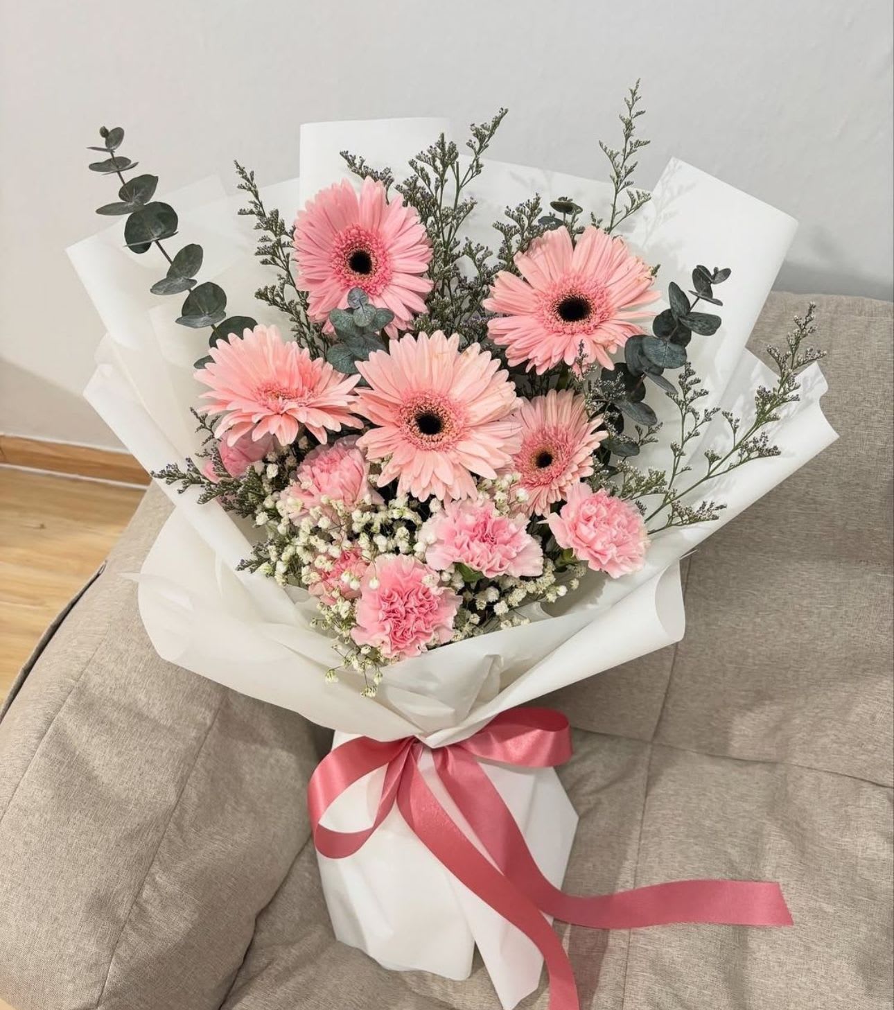 Pink gerbera daisy bouquet wrapped in white paper with a pink ribbon