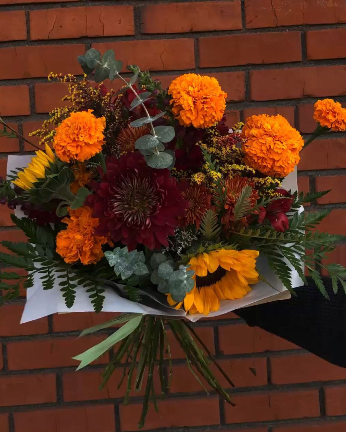 Bouquet of orange marigolds, sunflowers, and dark red blooms