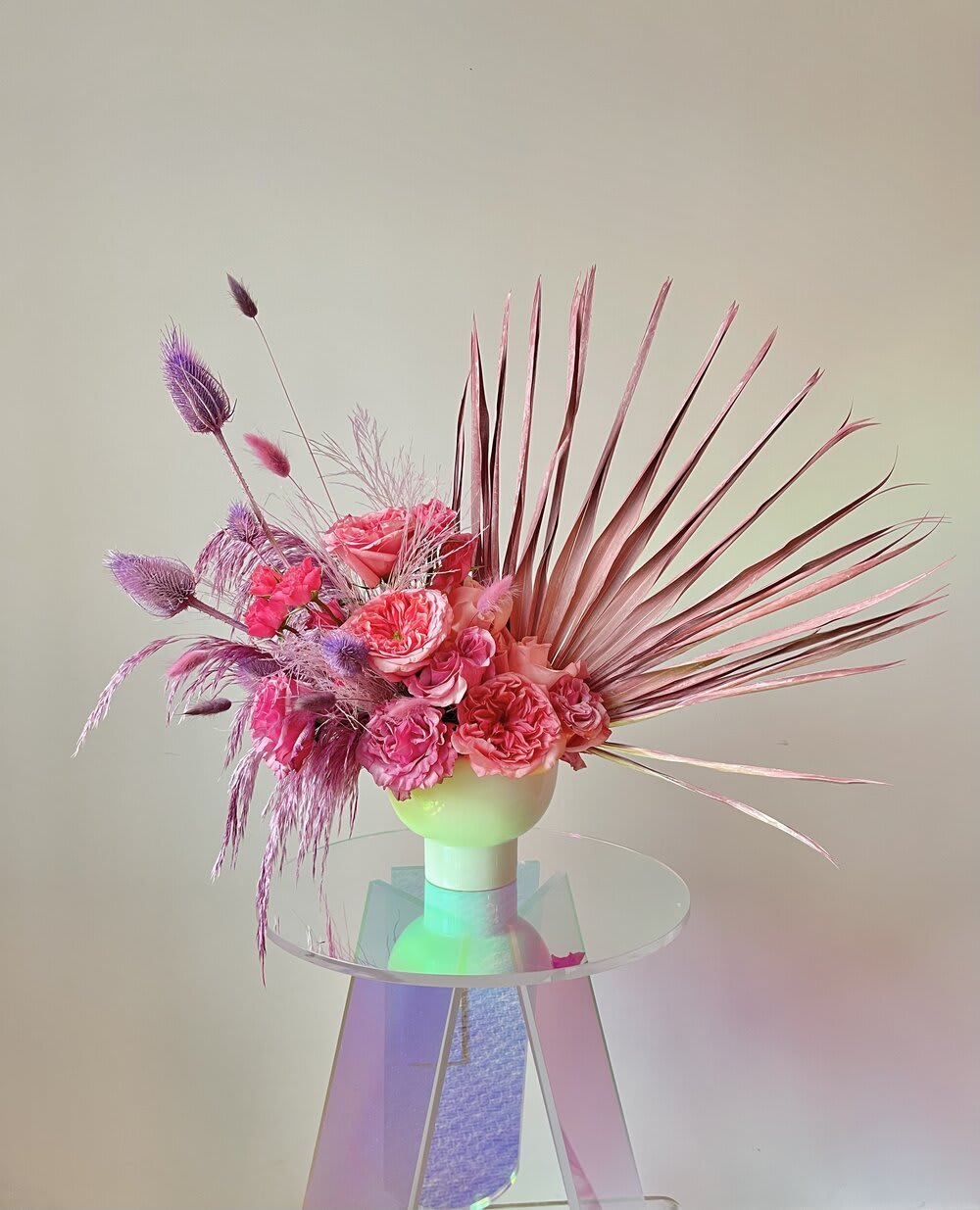 Pink and purple floral arrangement in a white vase with fan-like palm fronds