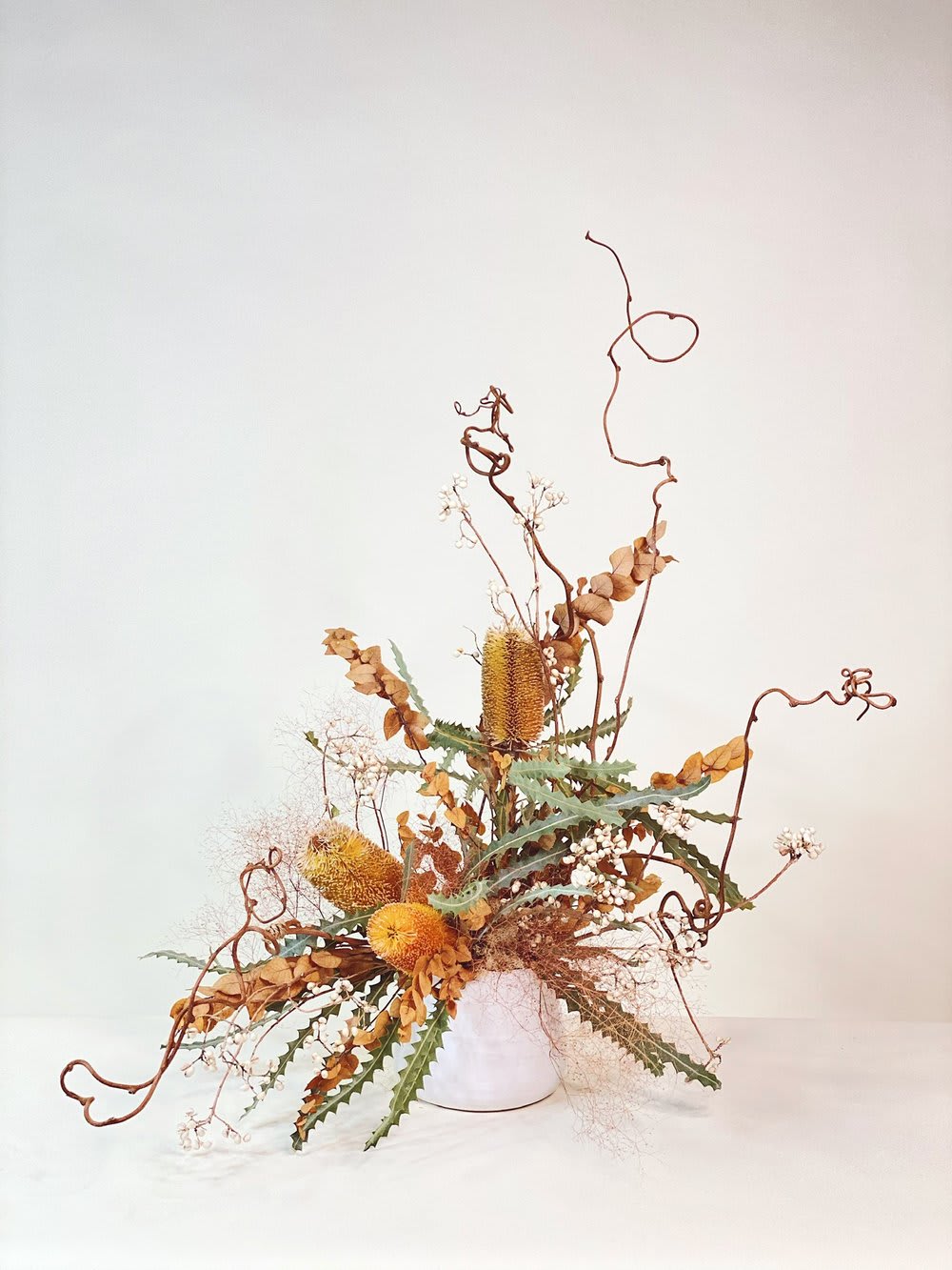 Tall dried floral arrangement in a white vase with curling branches