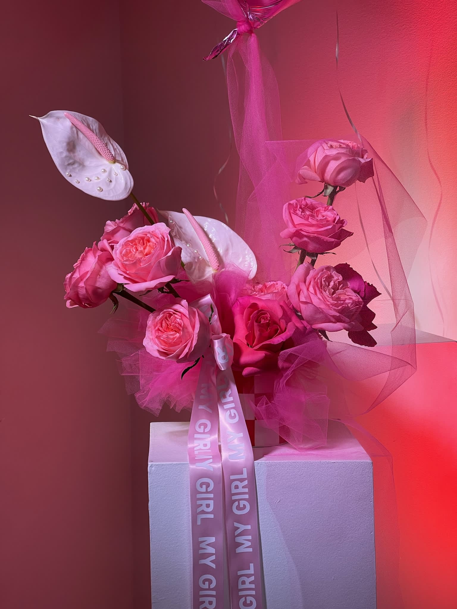 Pink rose arrangement with white anthuriums and a ribbon on a pedestal