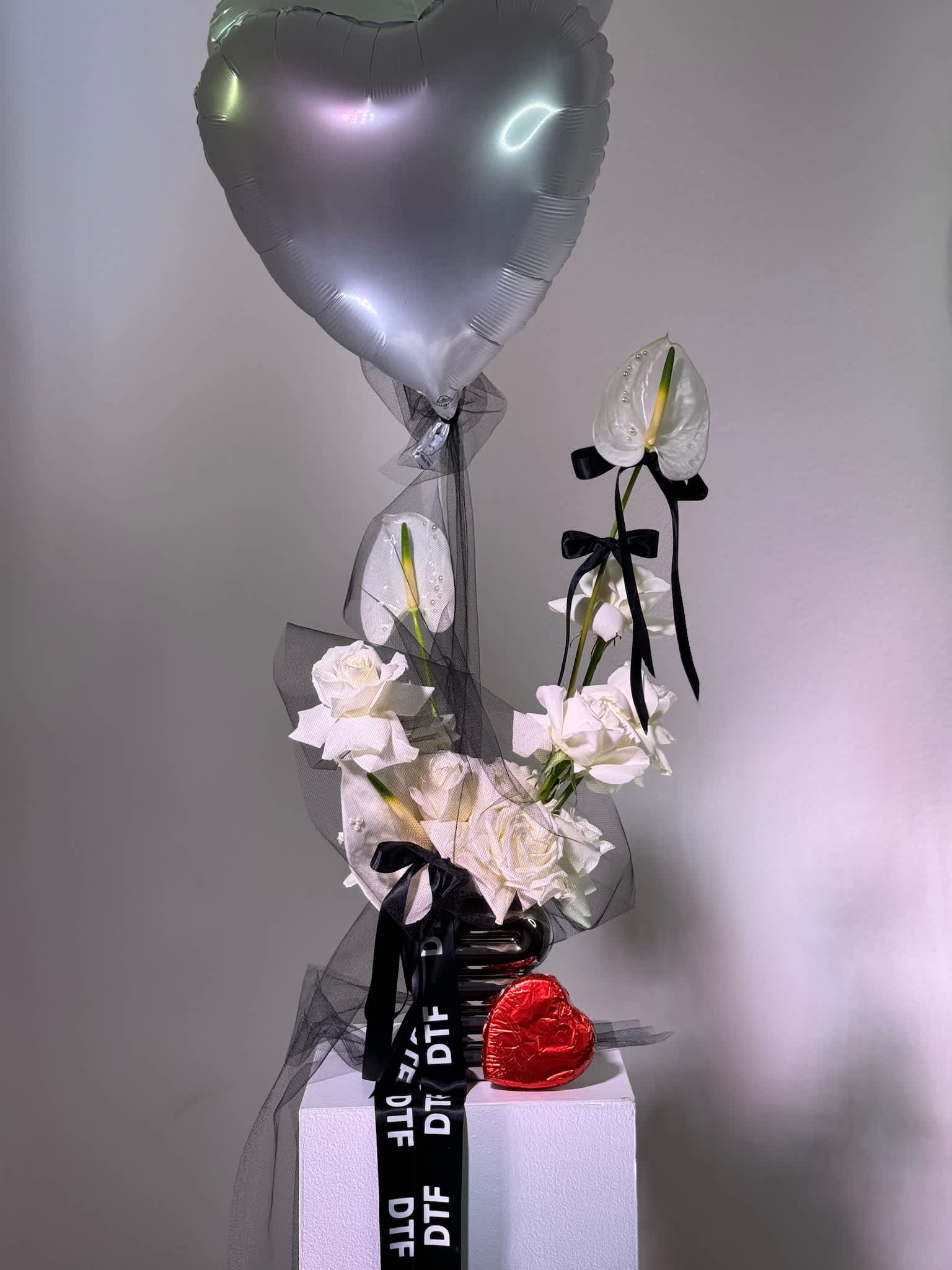 White roses with an anthurium and silver heart balloon on a pedestal