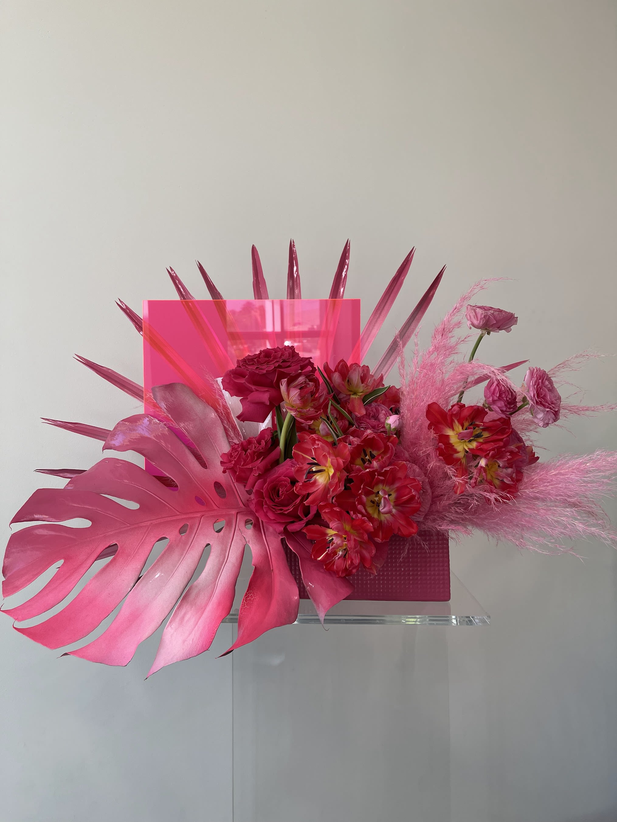 Pink floral arrangement with tropical leaves and a clear vase