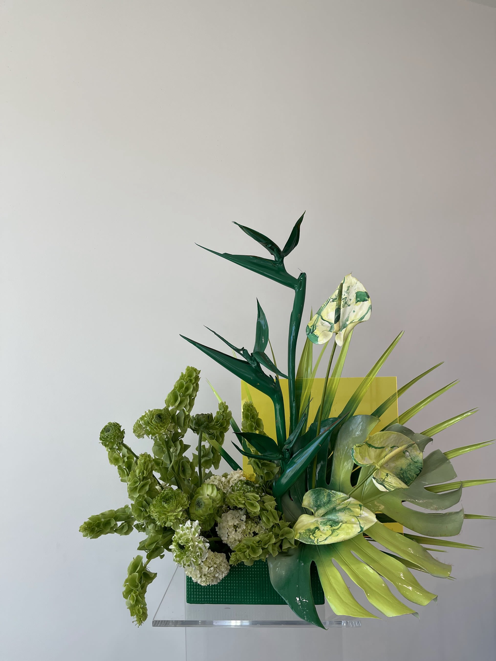 Green floral arrangement with tropical leaves and pale blooms in a square vase