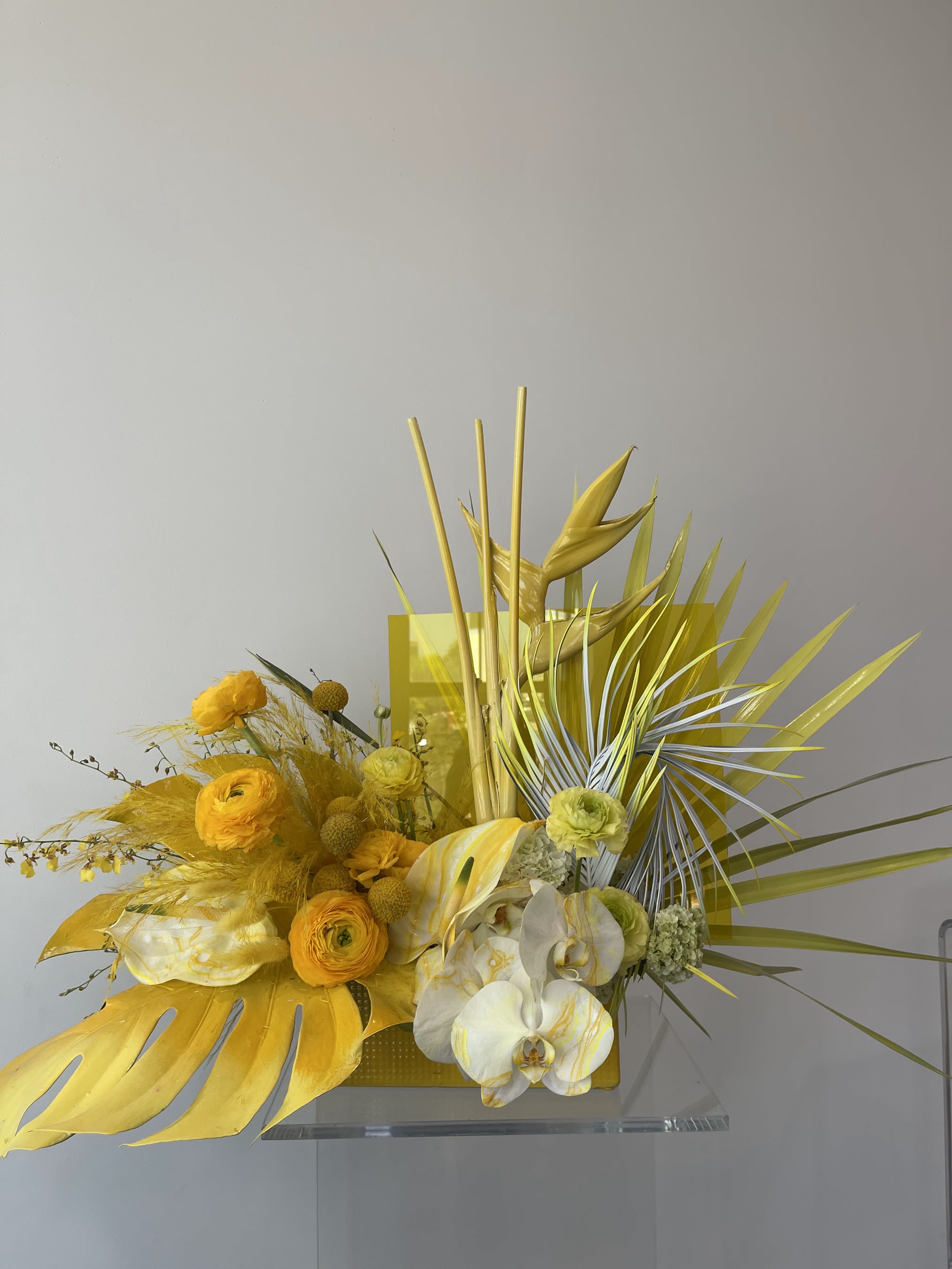 Yellow floral arrangement with orchids and tropical leaves in a rectangular container