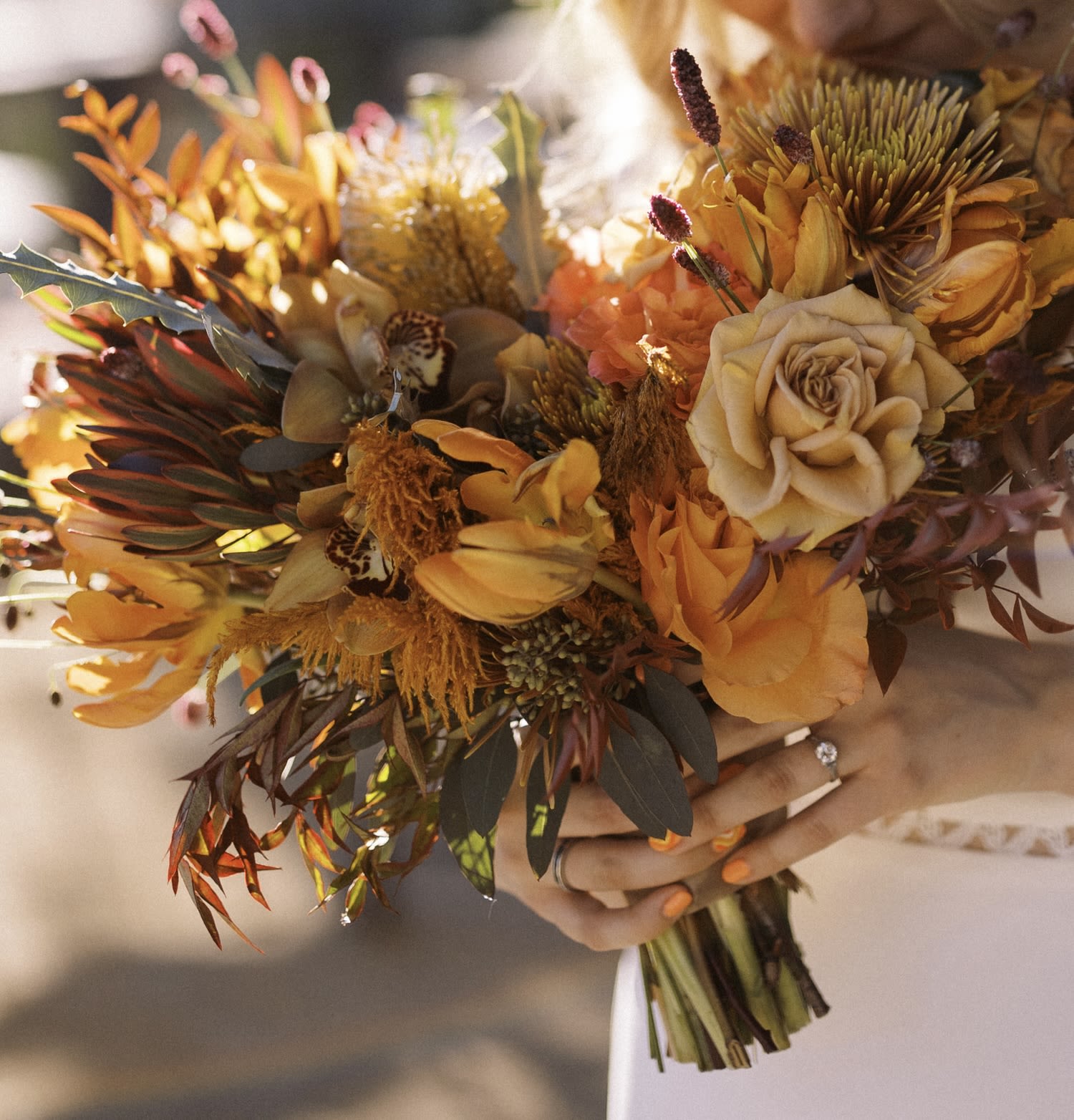 Handheld bouquet of orange and cream flowers with dark foliage