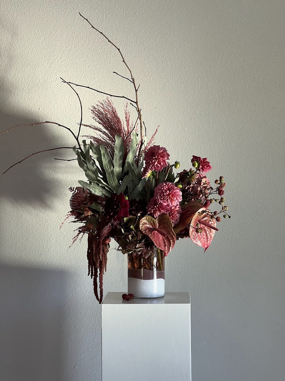 Tall burgundy floral arrangement in a glass vase with branching stems