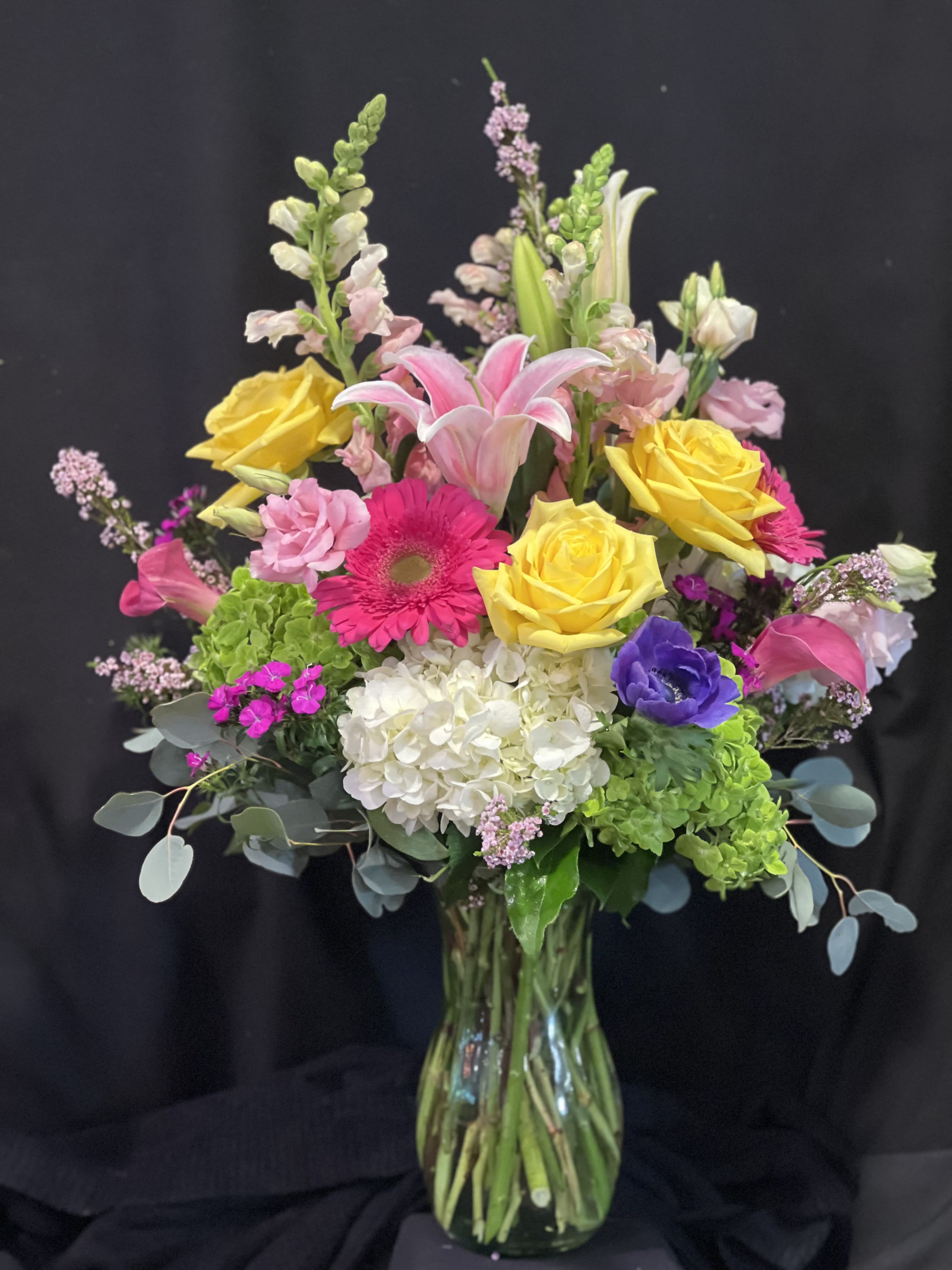 Mixed bouquet of roses, lilies, and gerbera daisies in a glass vase