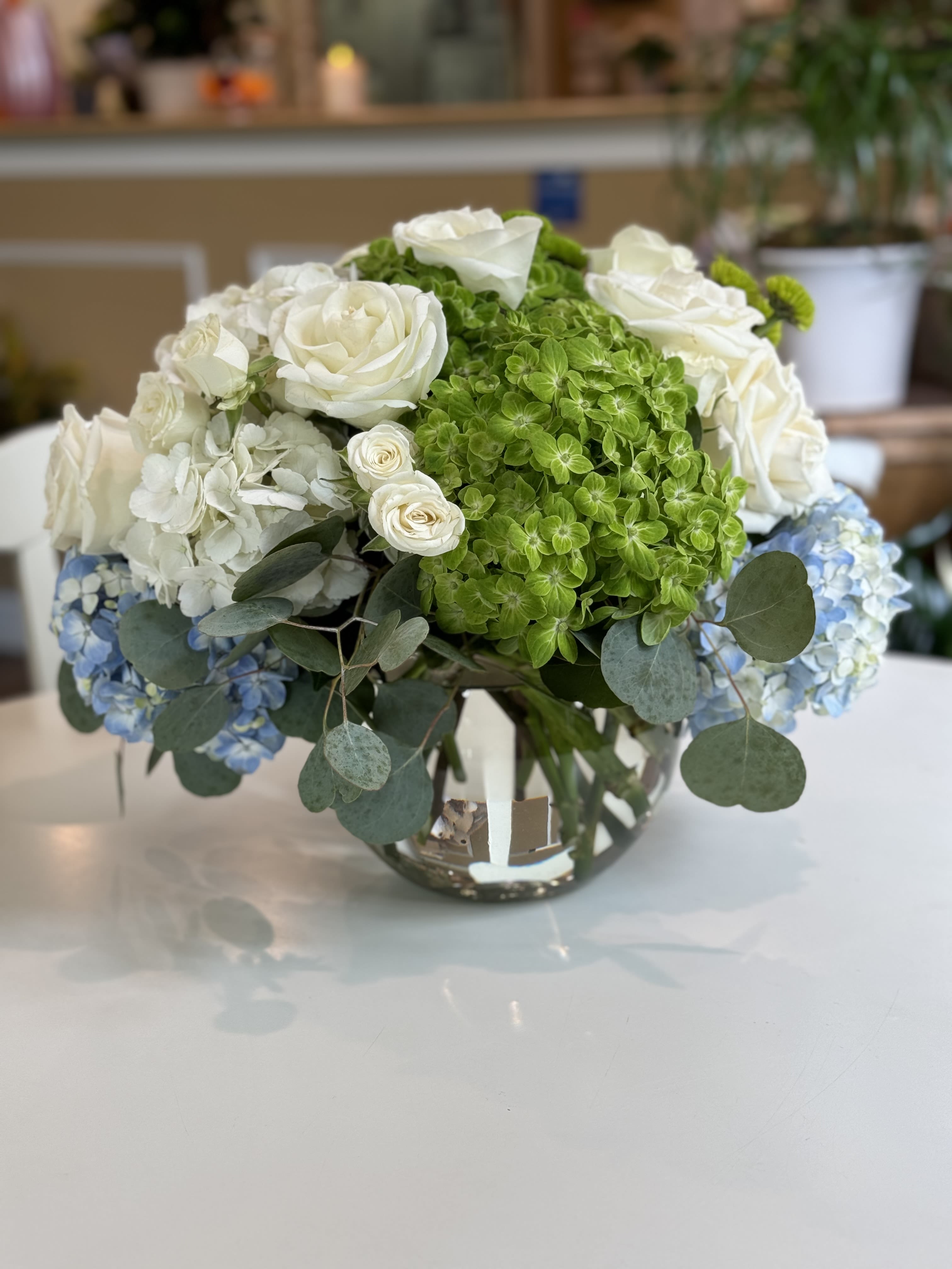 White roses and green hydrangeas in a glass vase with blue hydrangea accents