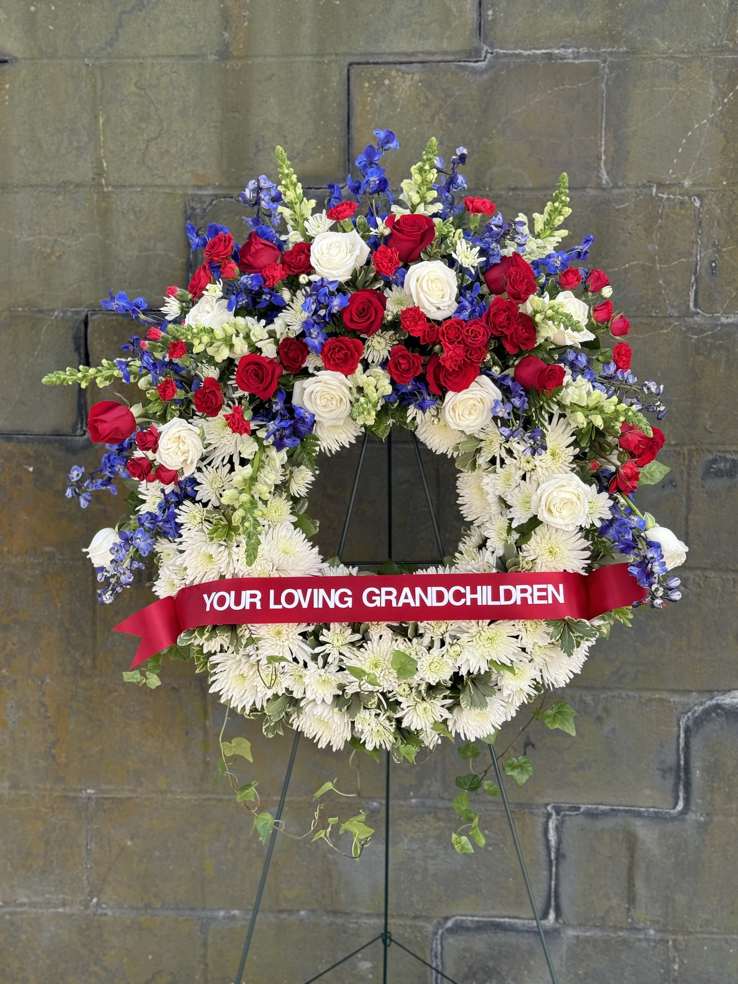 Large funeral wreath of red, white, and blue flowers on an easel
