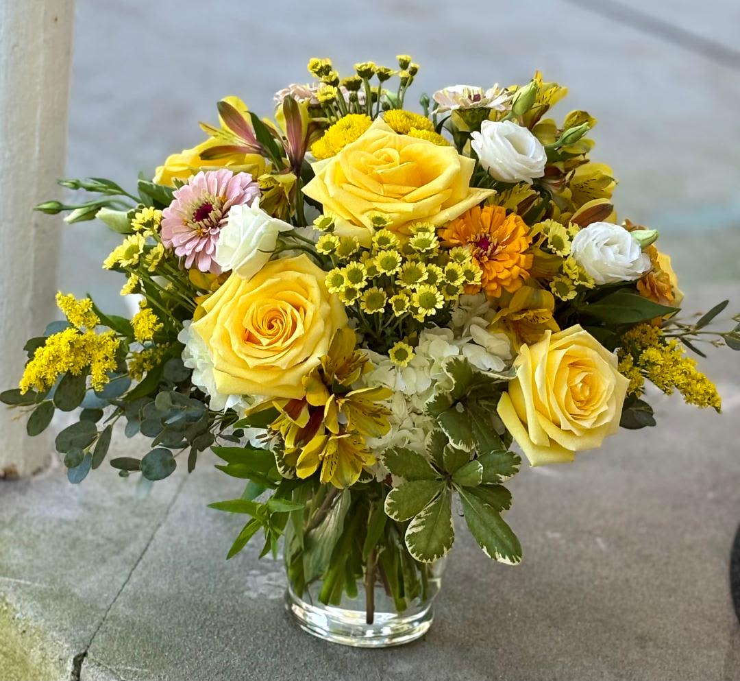Yellow roses and mixed flowers arranged in a clear glass vase