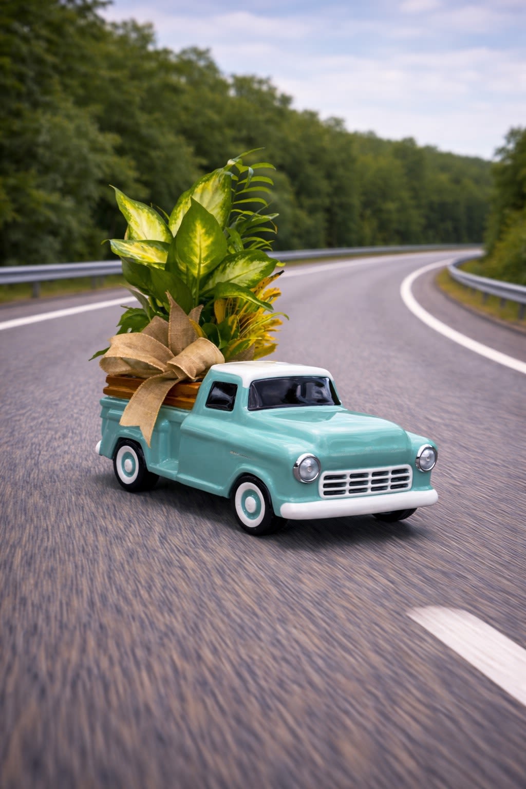 Mini turquoise pickup truck holding a potted leafy plant with a ribbon