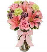 Pink lilies and roses arranged in a vase with a pink ribbon