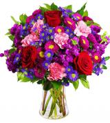 Bouquet of red roses, purple flowers, and pink carnations in a glass vase