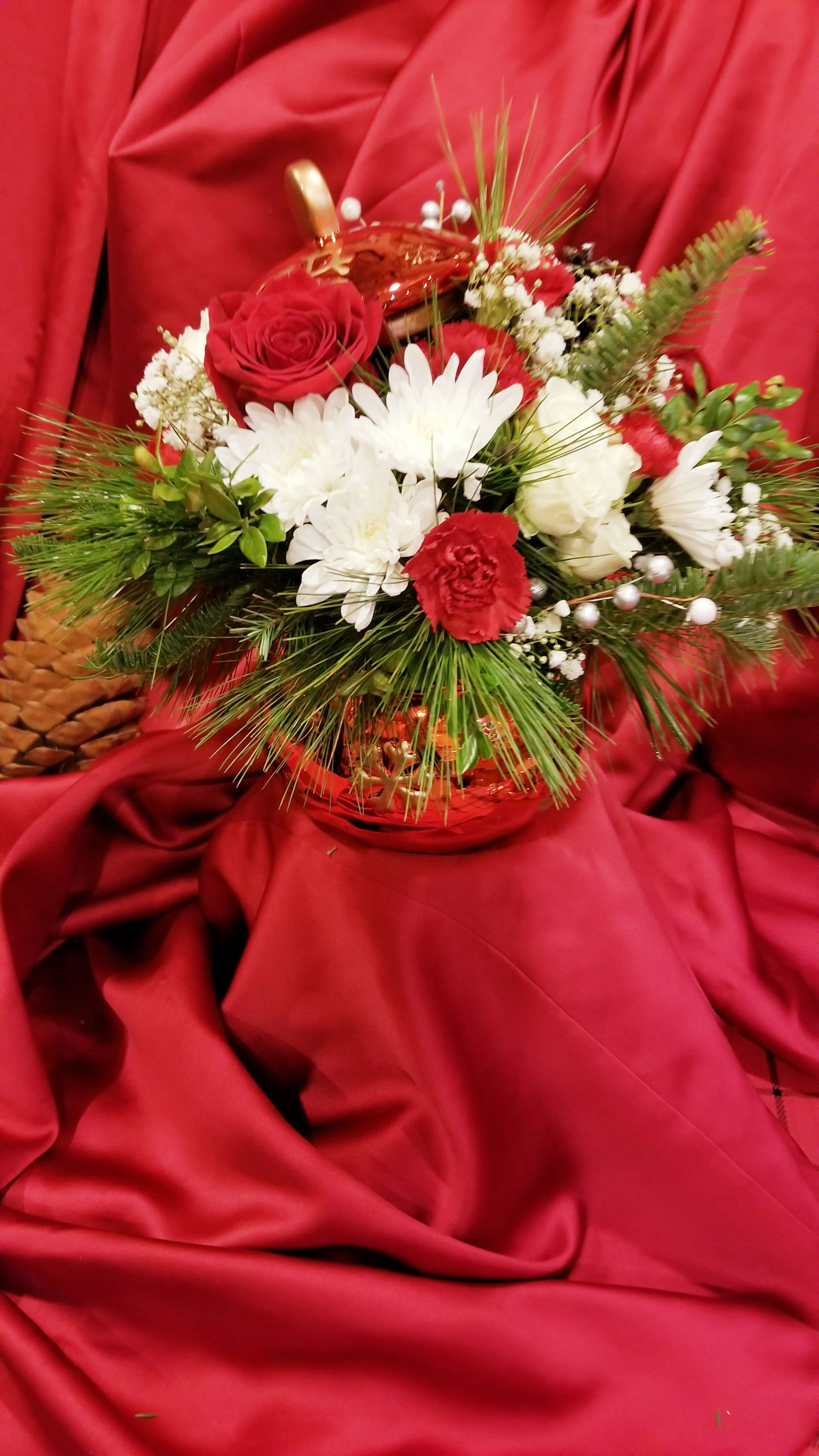 Red and white floral arrangement in a gold basket on red fabric