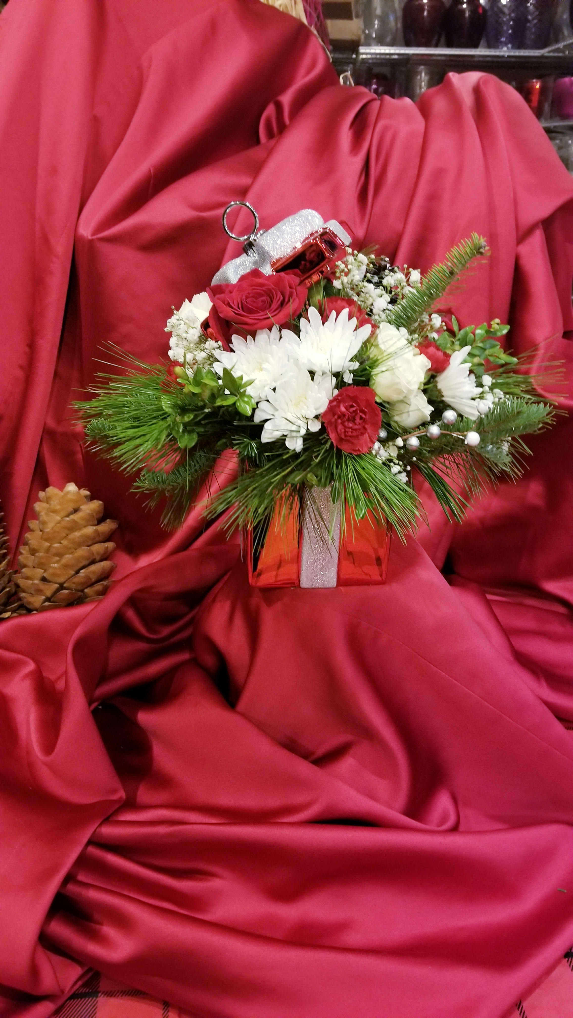 Holiday floral arrangement in a red gift box with a small ornament