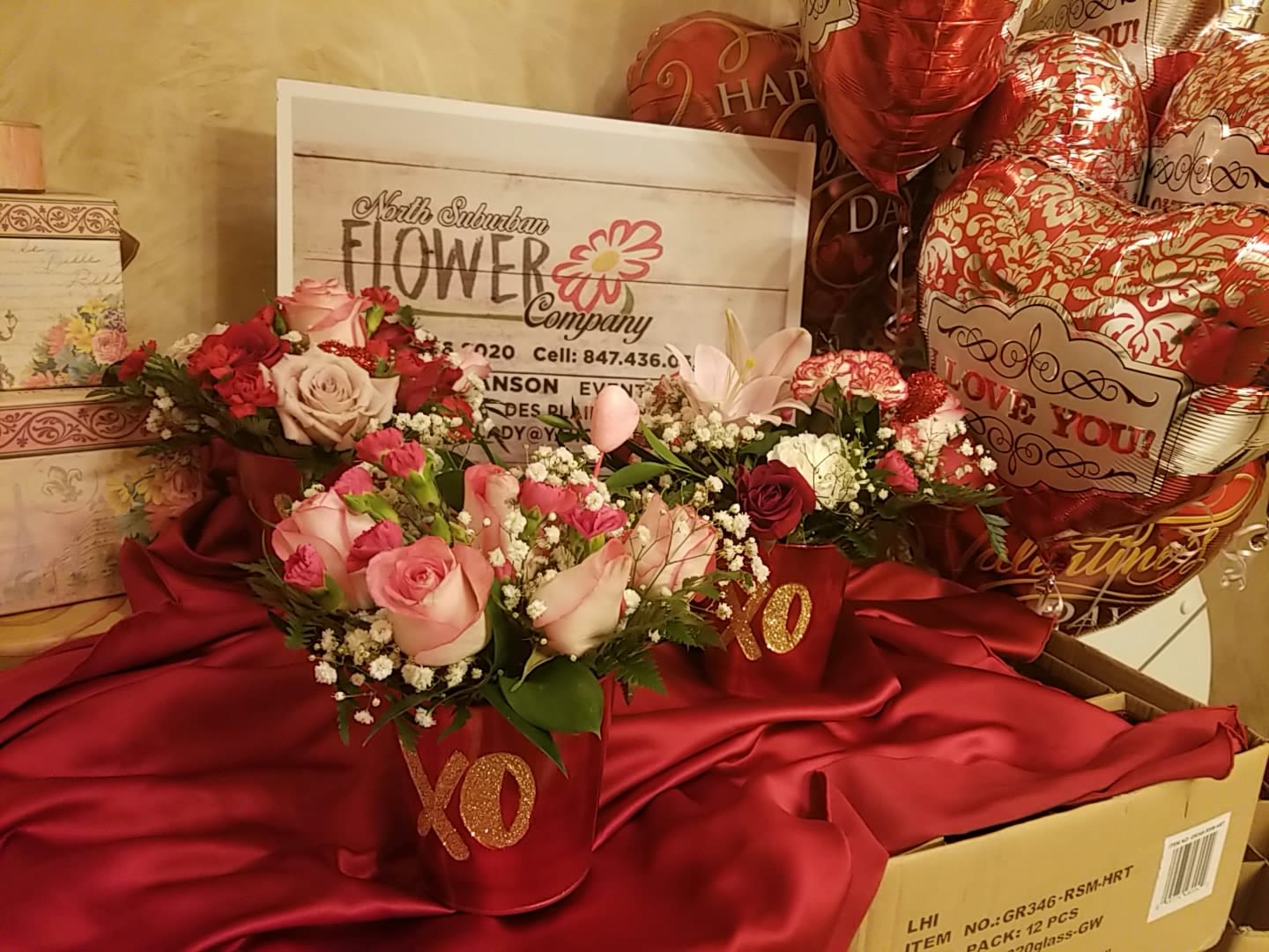 Pink and red rose arrangements in red XO containers with heart balloons