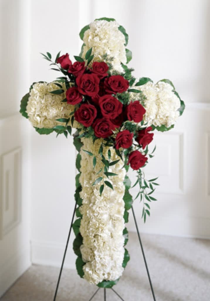 Cross-shaped floral tribute with red roses and white flowers on a stand