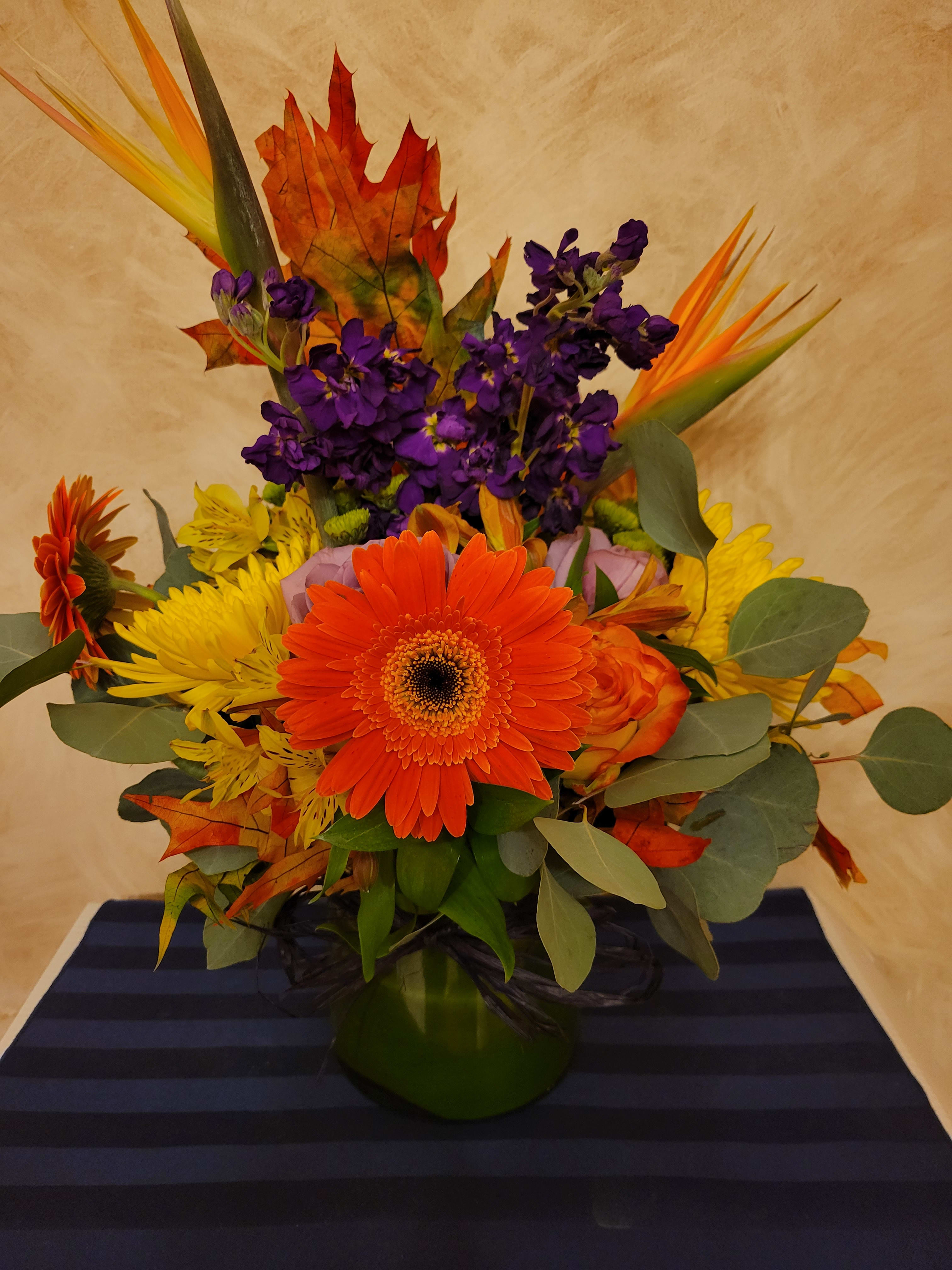 Bright mixed bouquet with orange gerbera daisies and purple flowers in a green vase