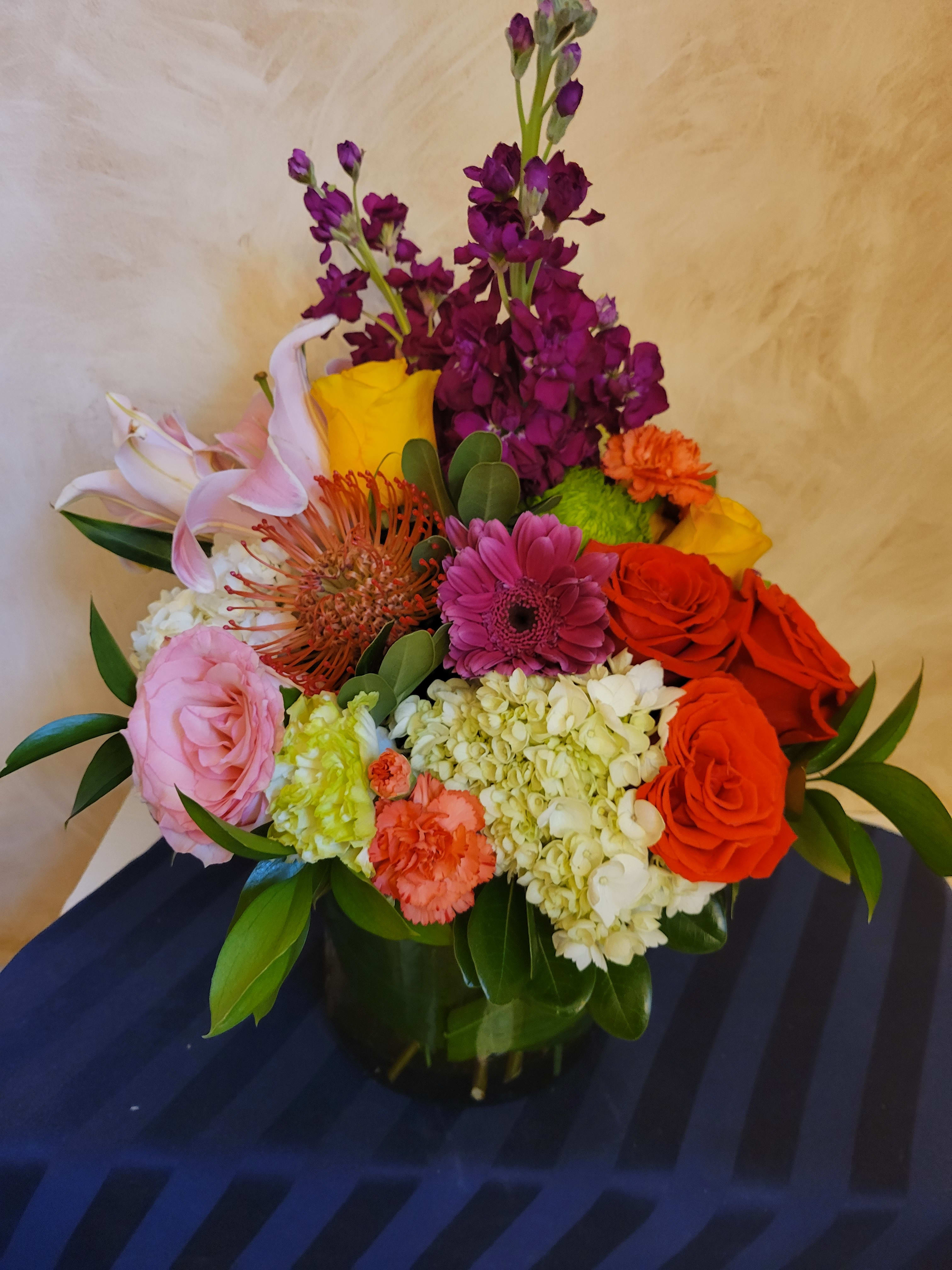 Mixed bouquet in a dark vase with roses, lilies, hydrangea, and bright accent flowers