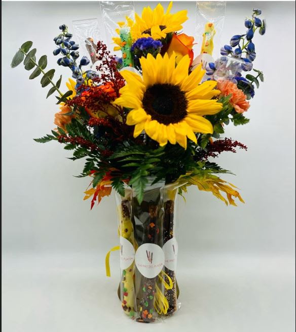 Bouquet with sunflowers, blue flowers, and orange blooms in a clear vase