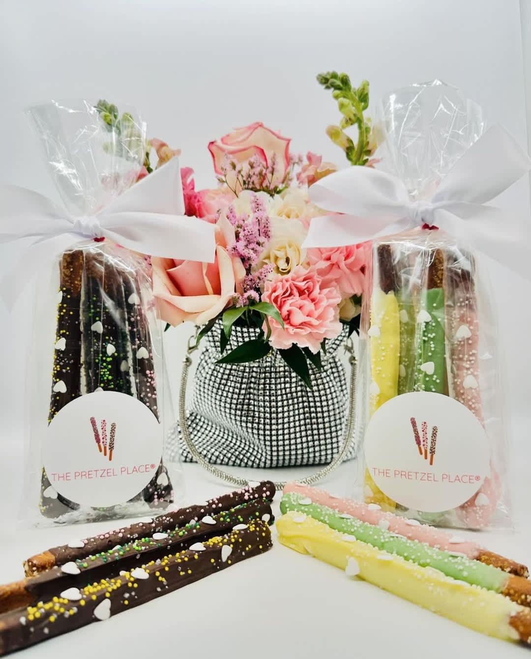 Flower arrangement with pink and peach roses beside wrapped chocolate-covered pretzels