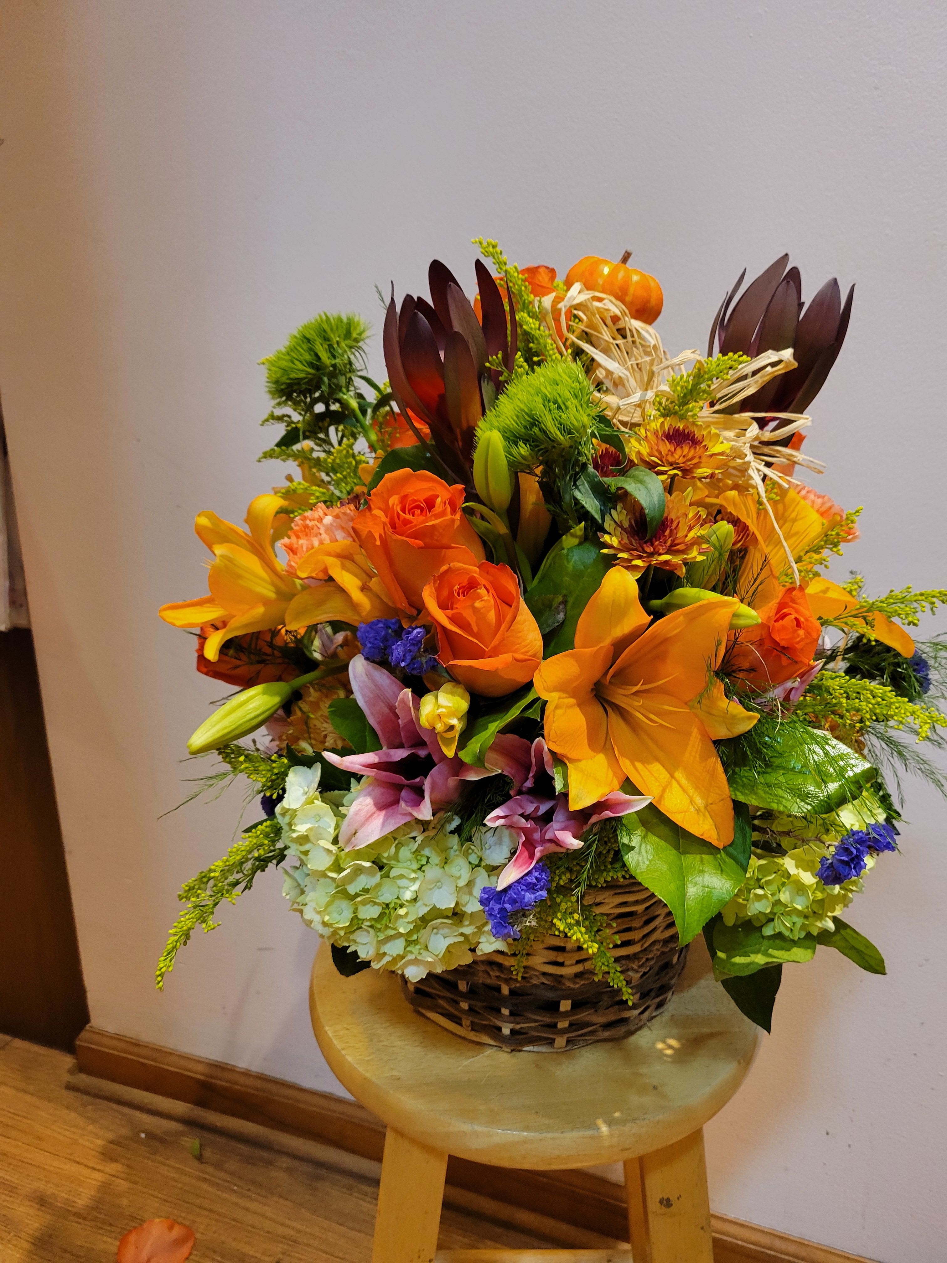 Basket arrangement with orange lilies, roses, and autumn accents