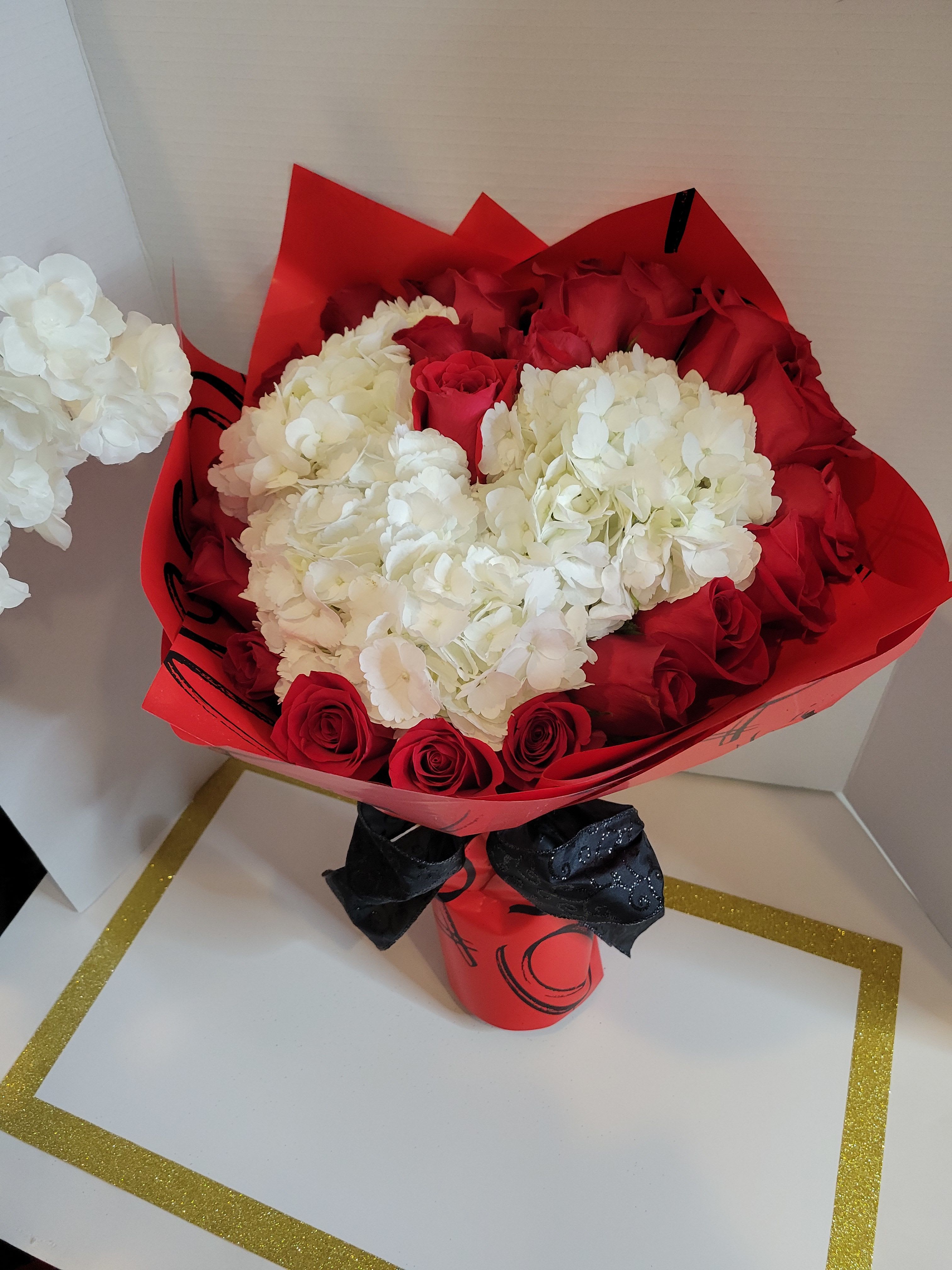 Red roses and white hydrangeas wrapped in red paper with a black ribbon
