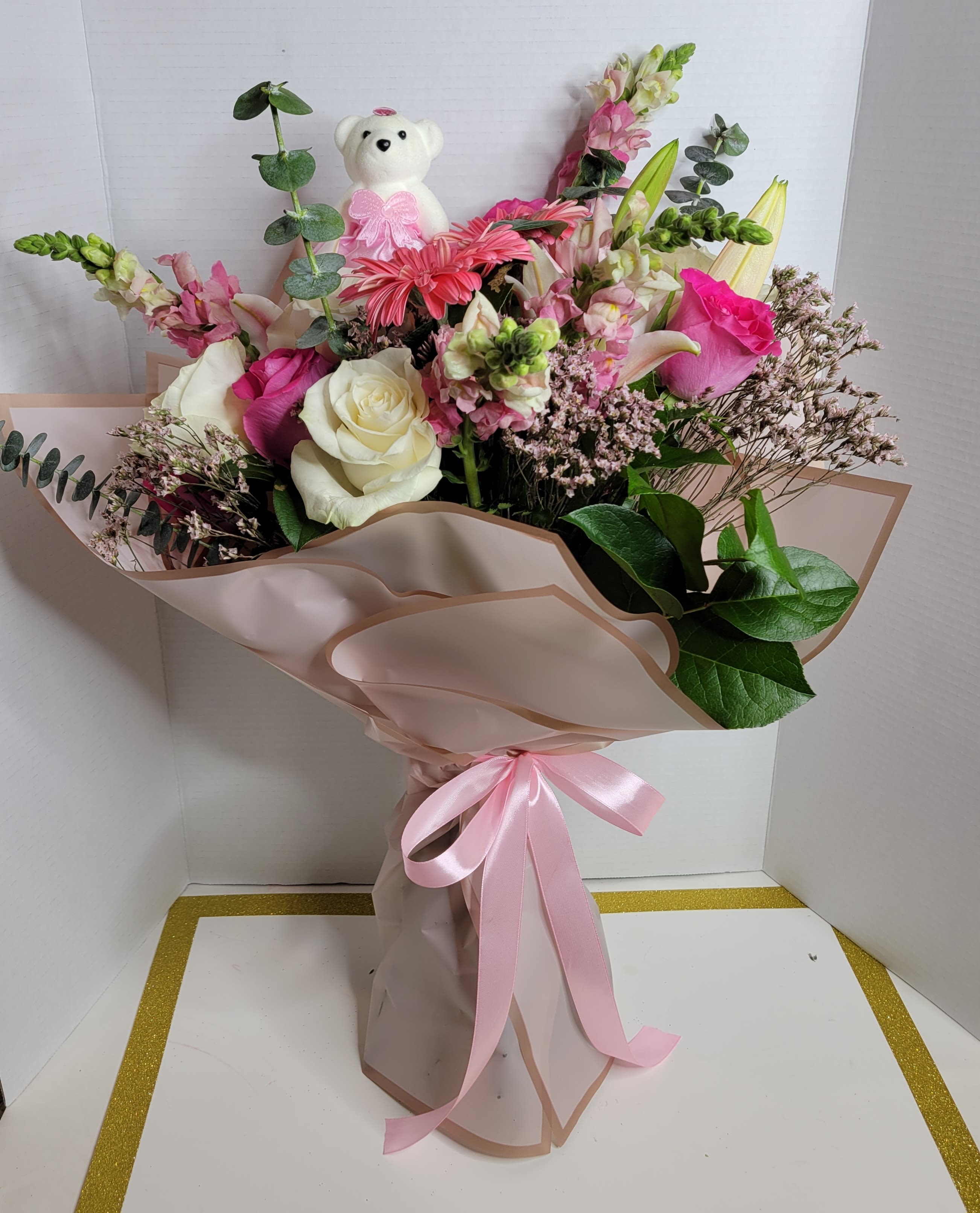 Pink and white bouquet with roses, lilies, and a teddy bear topper
