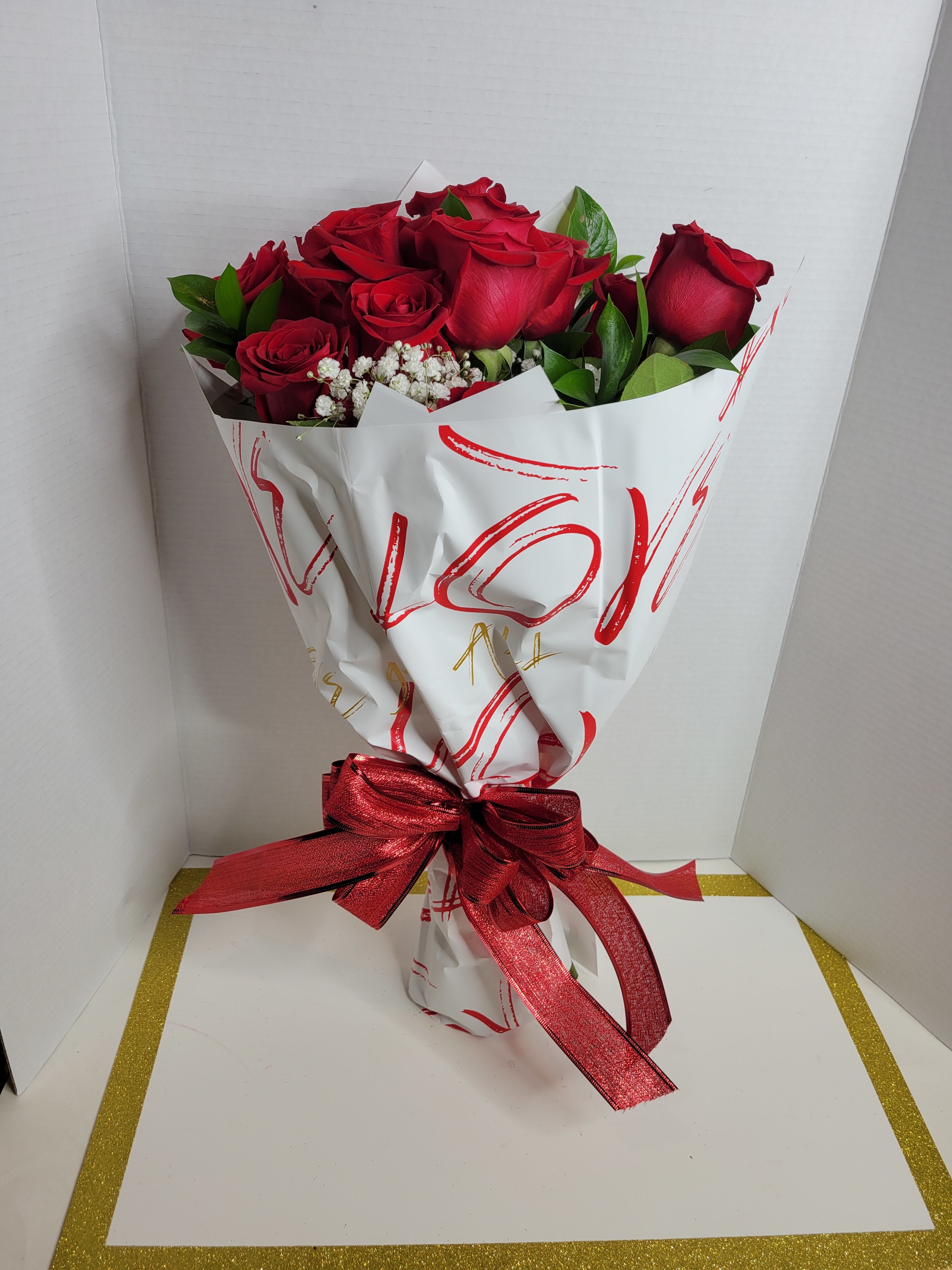 Bouquet of red roses with white filler flowers wrapped in white paper and a red ribbon