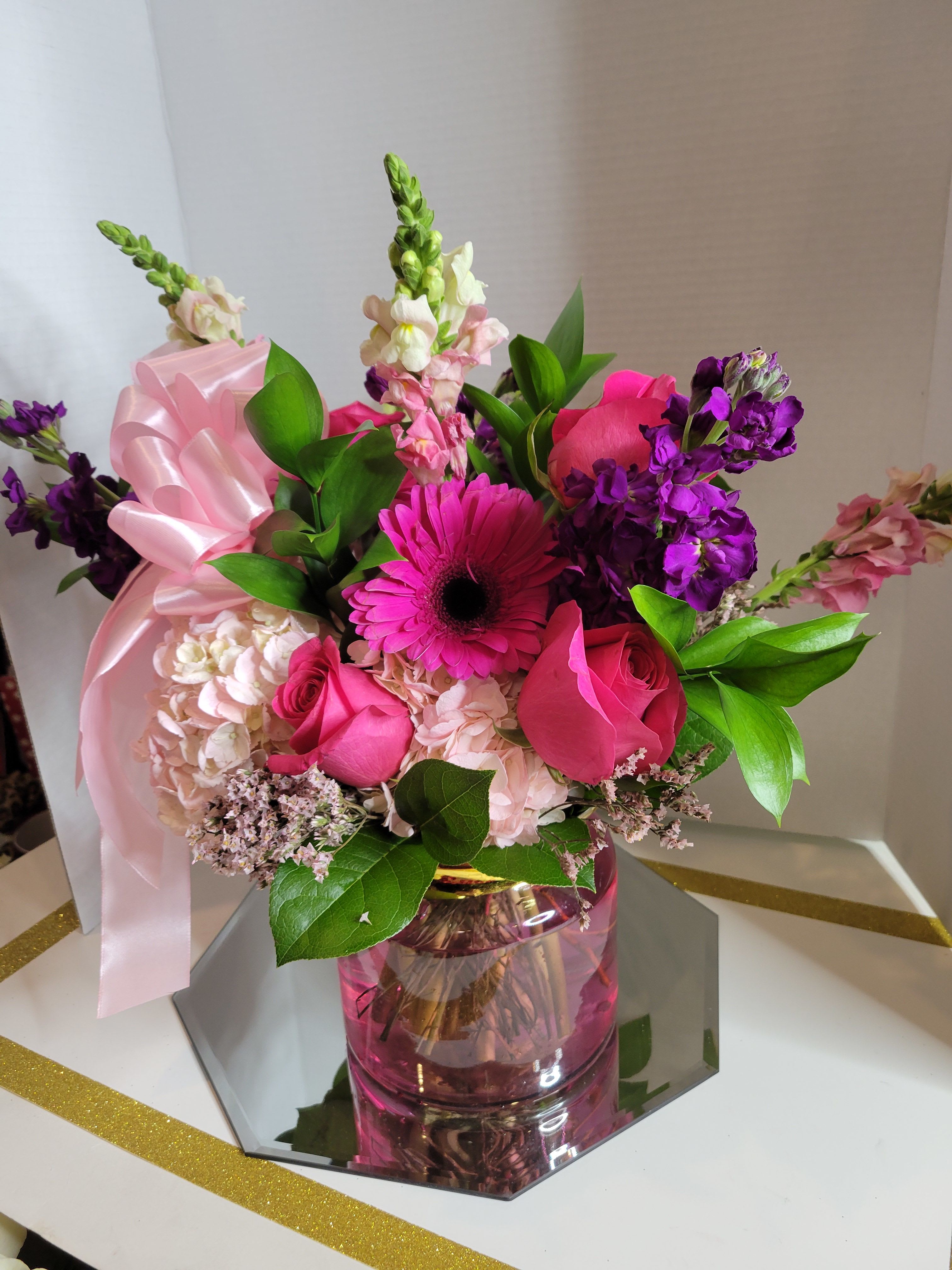 Pink and purple mixed bouquet in a pink glass vase with a ribbon
