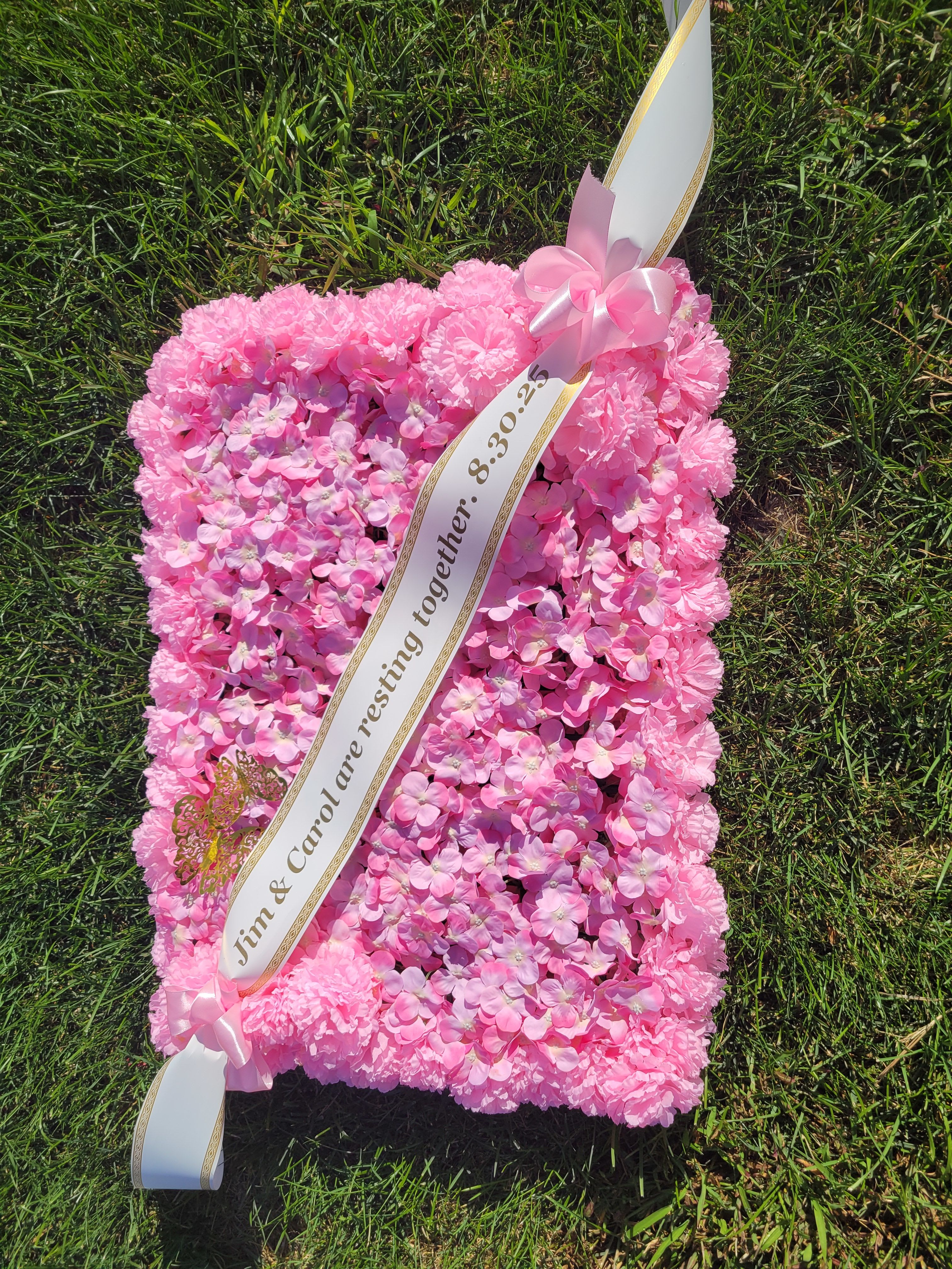 Pink floral sympathy pillow with ribbon sash on grass