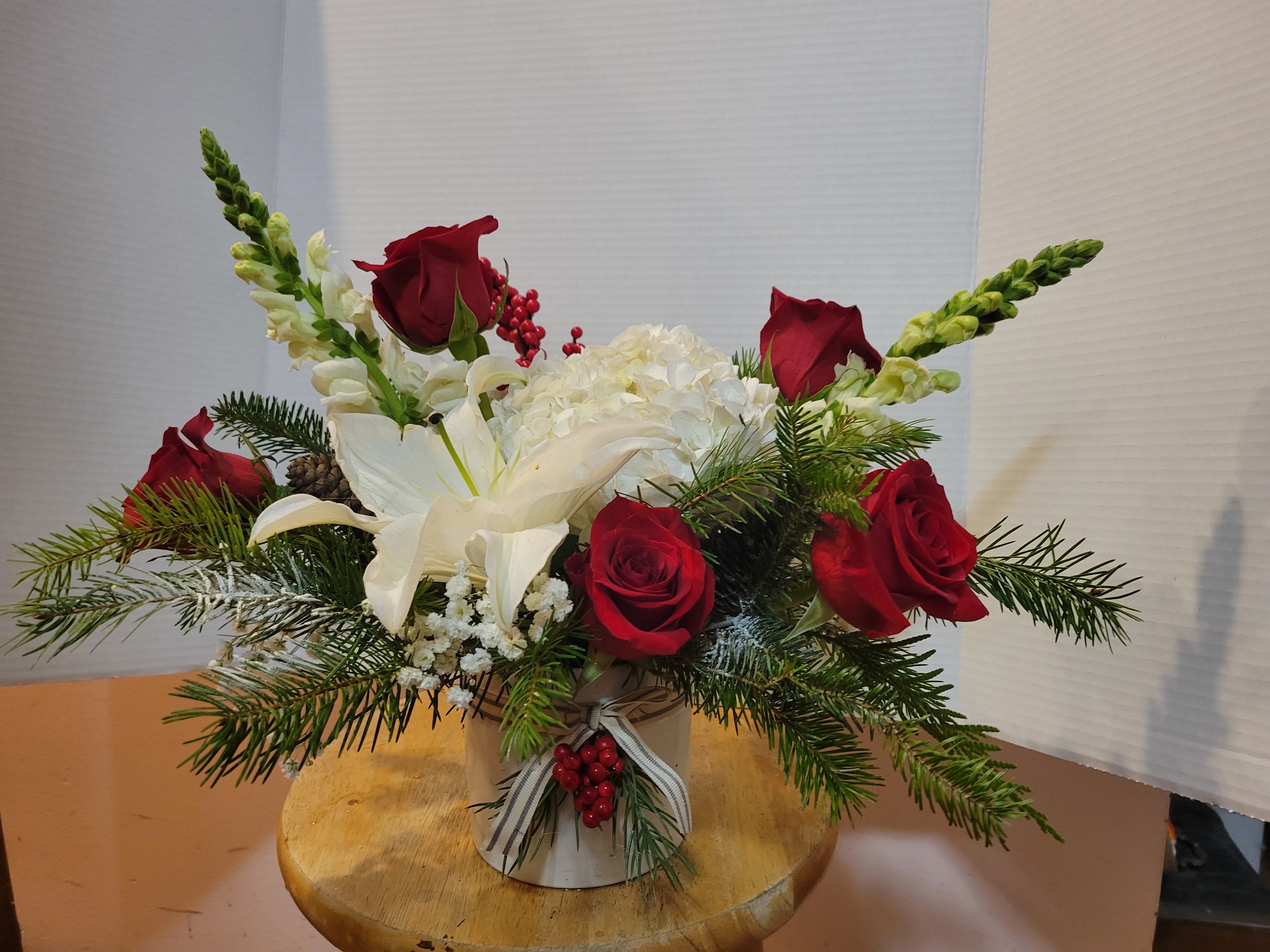 Red roses and white lilies in a small vase with evergreen accents