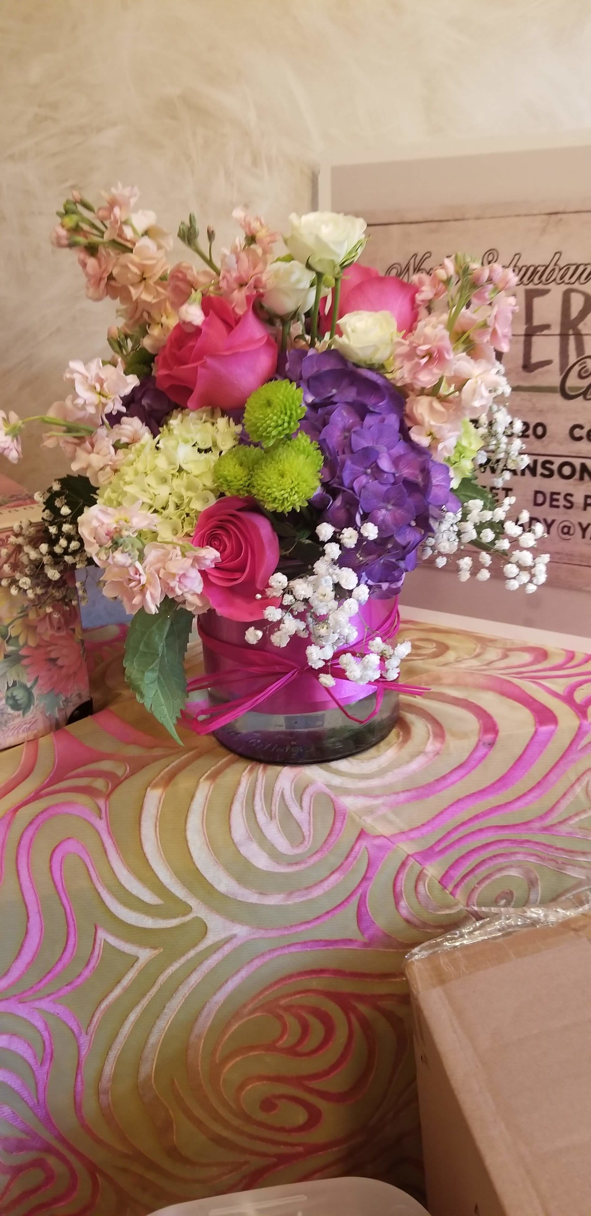 Pink, purple, and white flower arrangement in a round vase with a pink ribbon