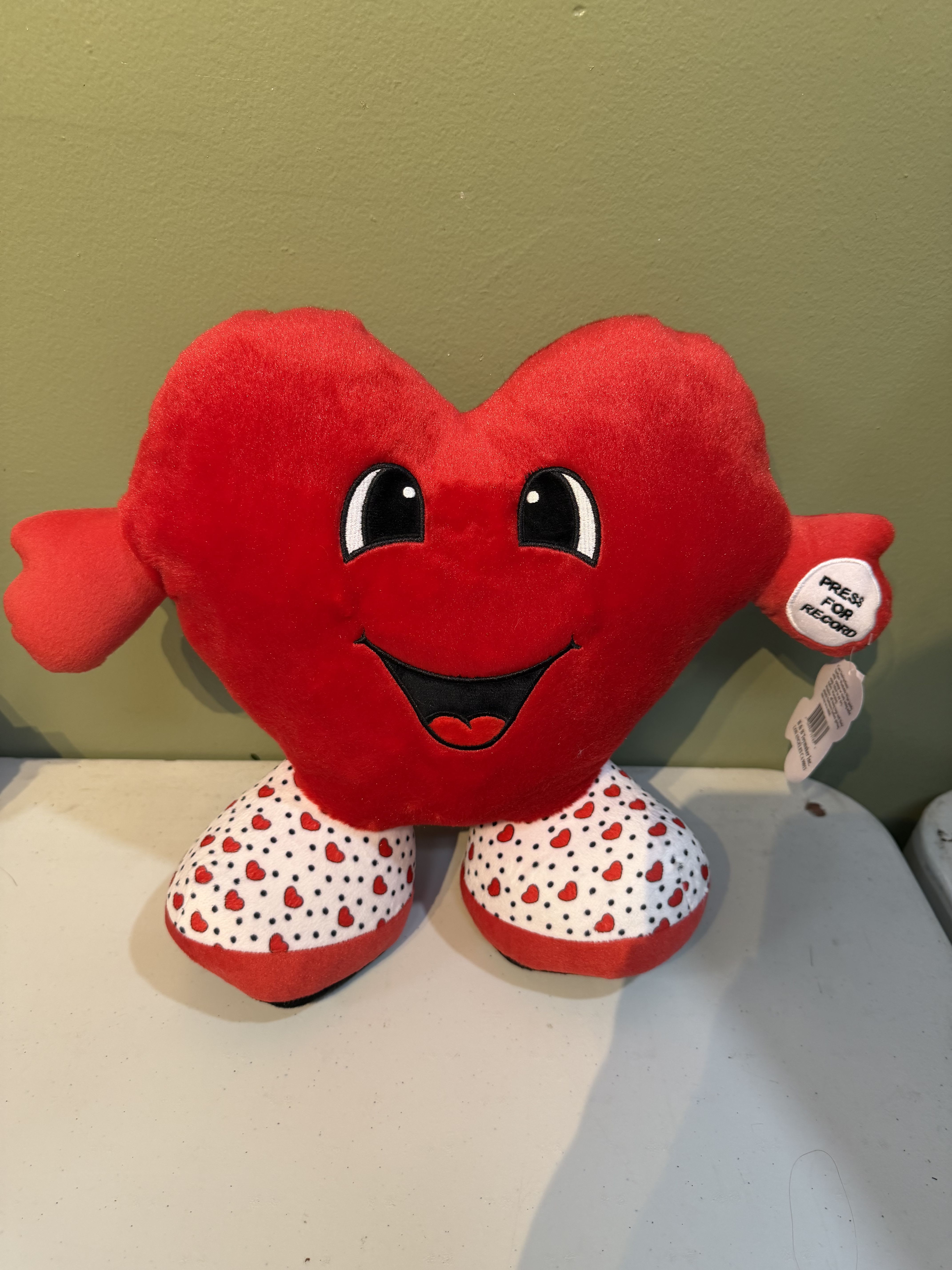 Red heart-shaped plush toy with a smiling face and patterned feet