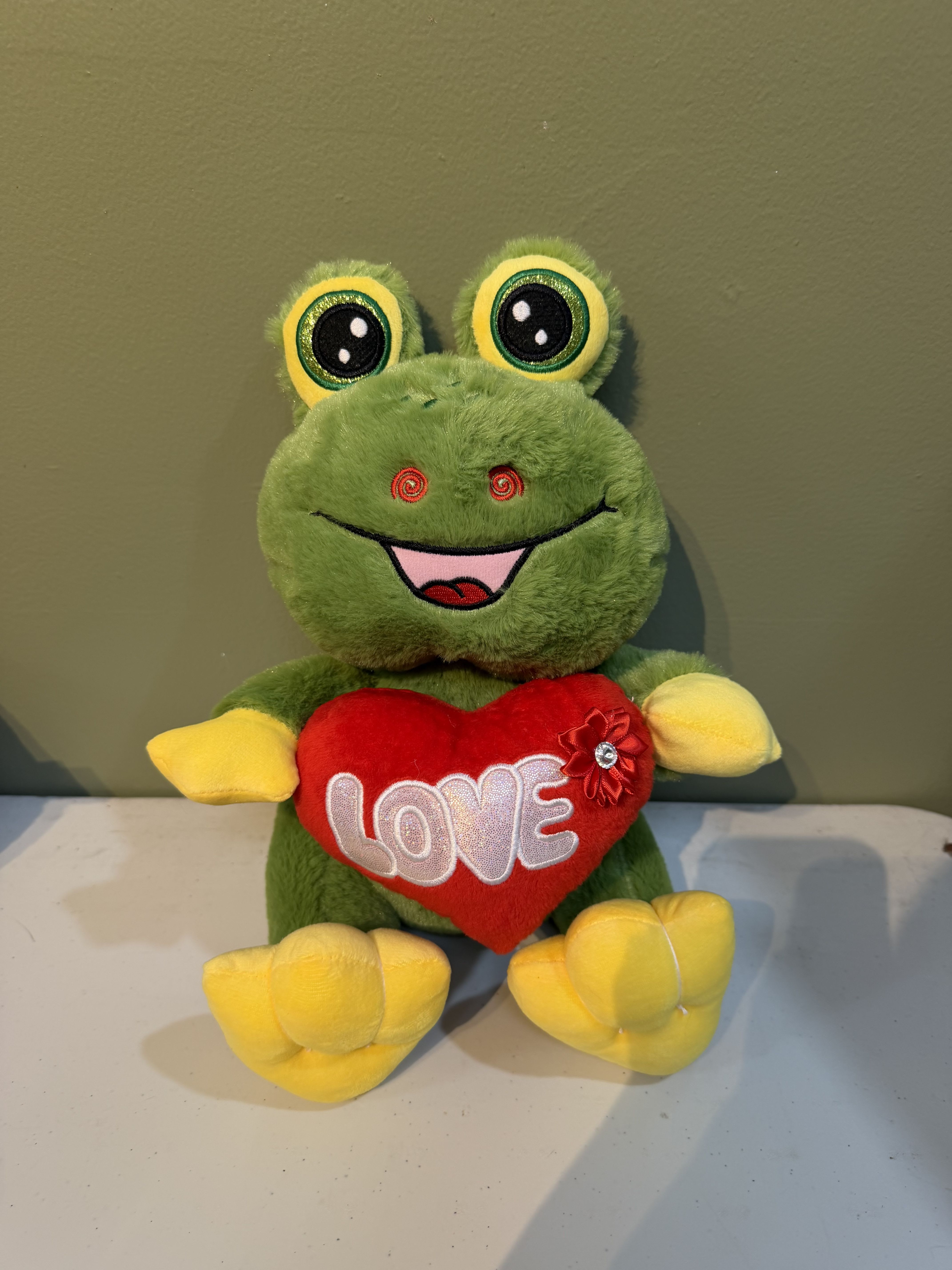 Plush green frog holding a red heart with the word LOVE