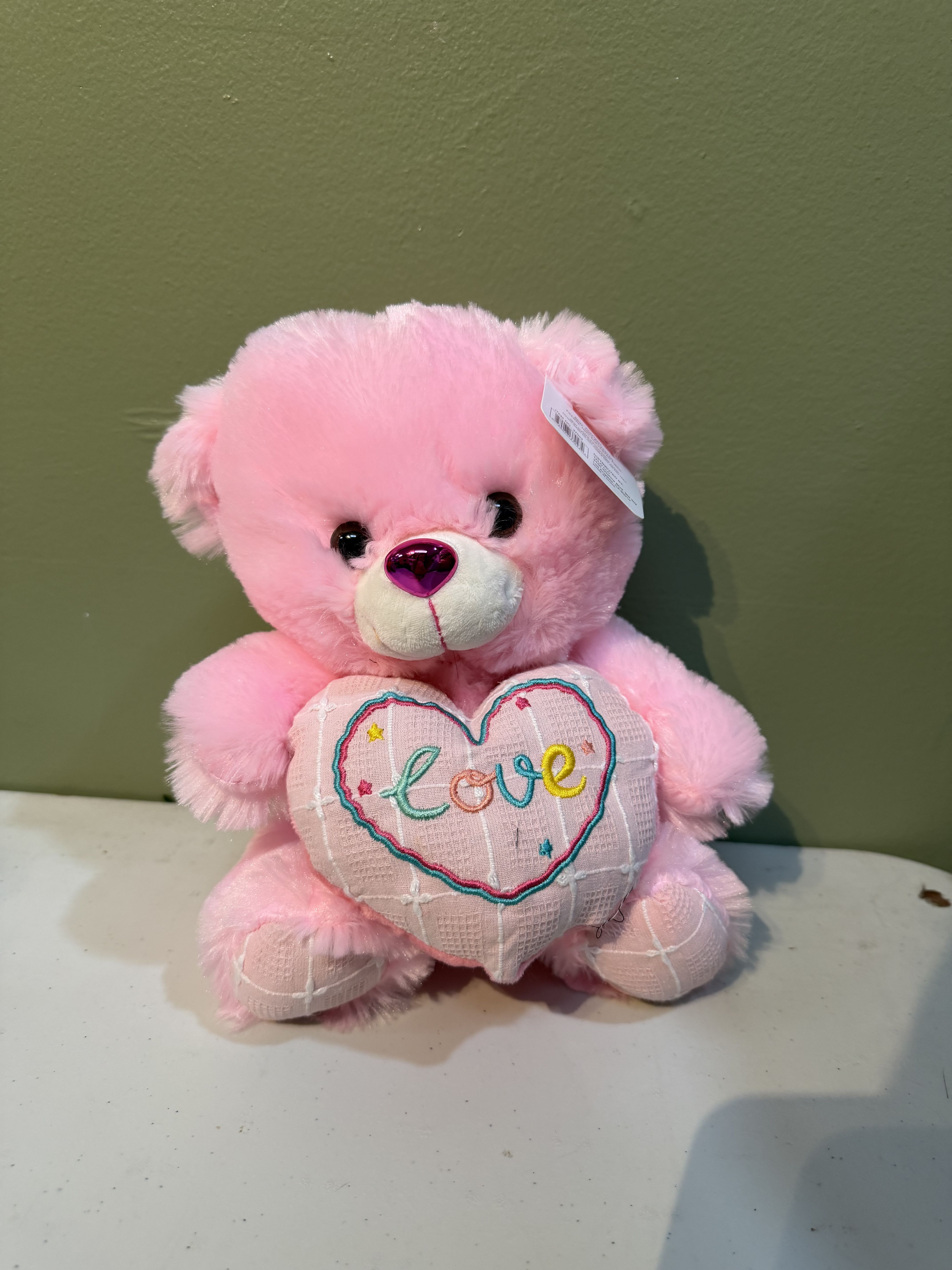 Pink teddy bear holding a heart with the word love