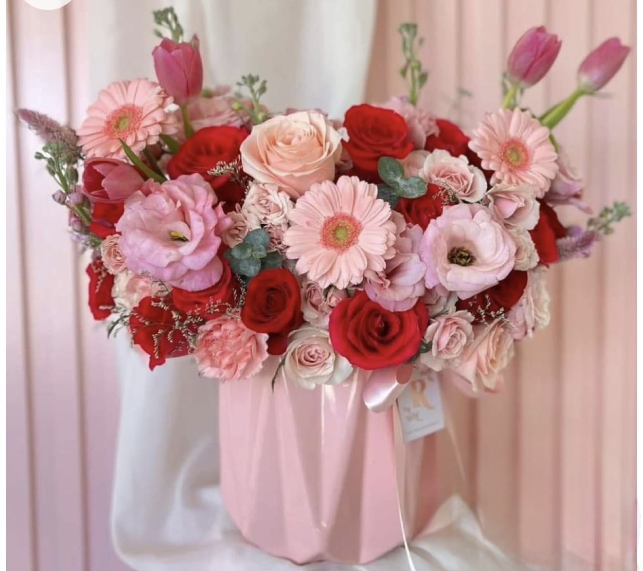 Pink and red bouquet with roses, gerbera daisies, and tulips in a pink wrap
