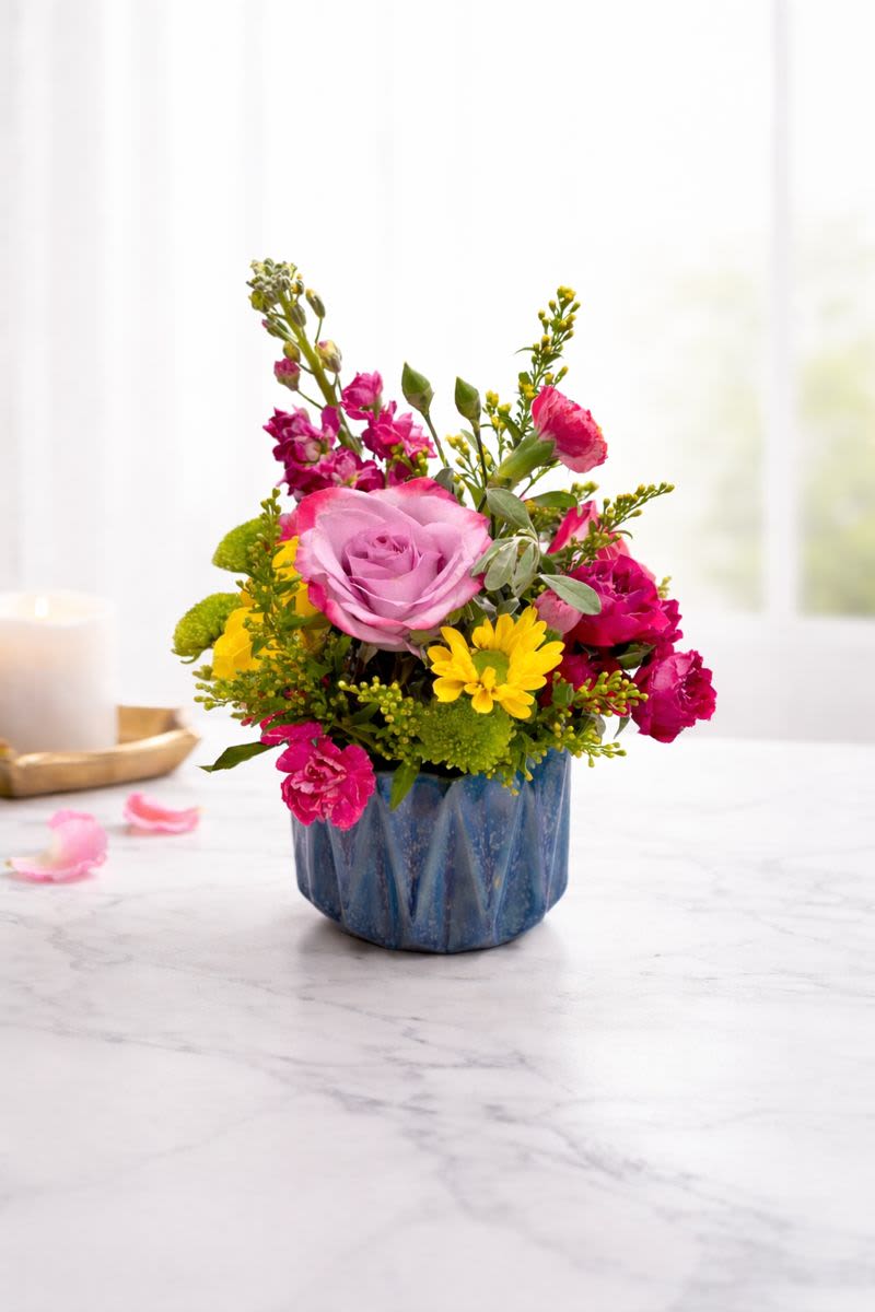 Pink and yellow flower arrangement in a blue ceramic pot