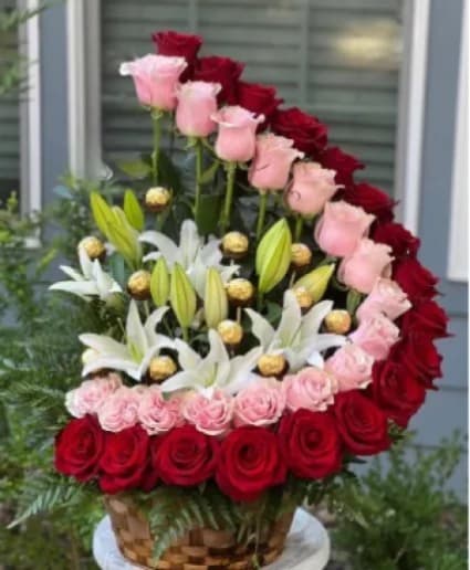 Heart-shaped floral arrangement with red and pink roses and white lilies in a basket