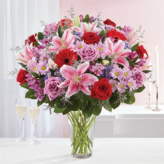 Mixed bouquet of pink lilies, red roses, and lavender flowers in a clear glass vase