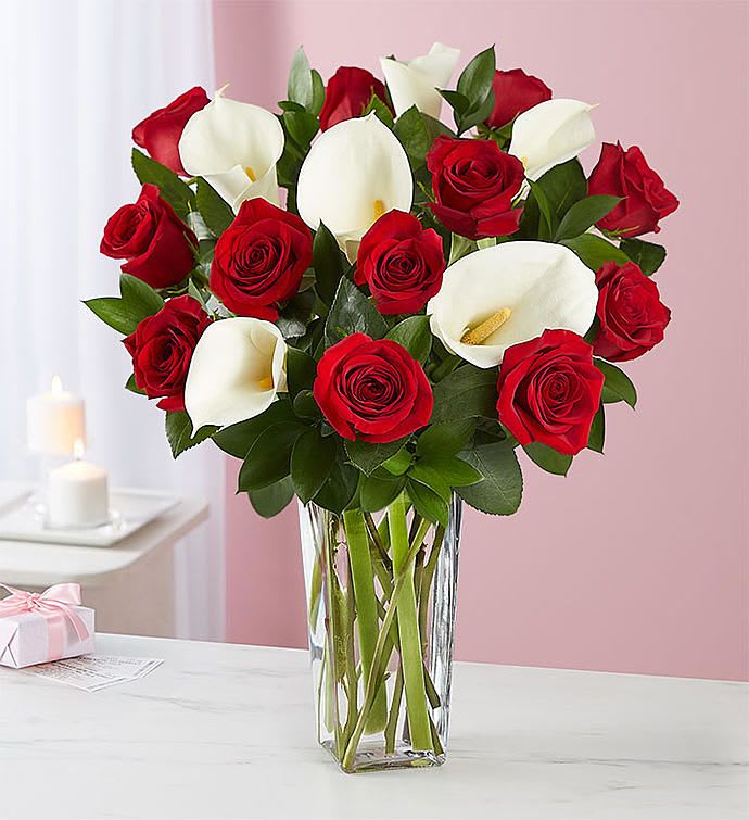 Red roses and white calla lilies arranged in a clear glass vase.