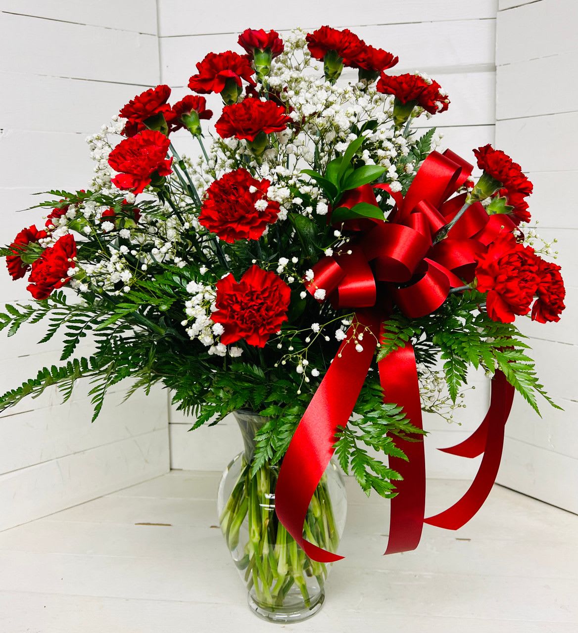 Red carnations and white baby's breath in a clear glass vase with a red ribbon