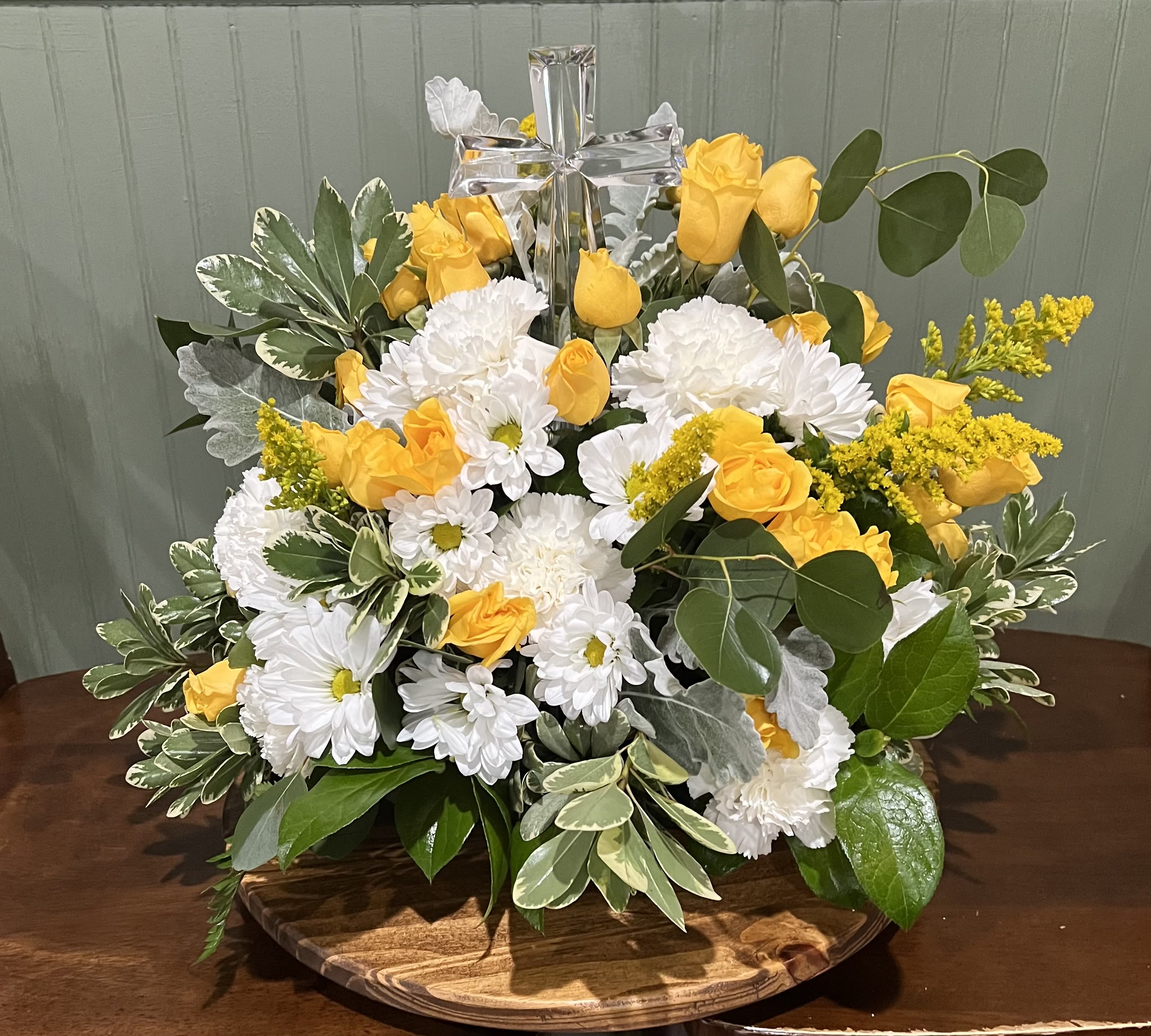 Yellow roses and white daisies arranged on a wooden tray with a silver cross