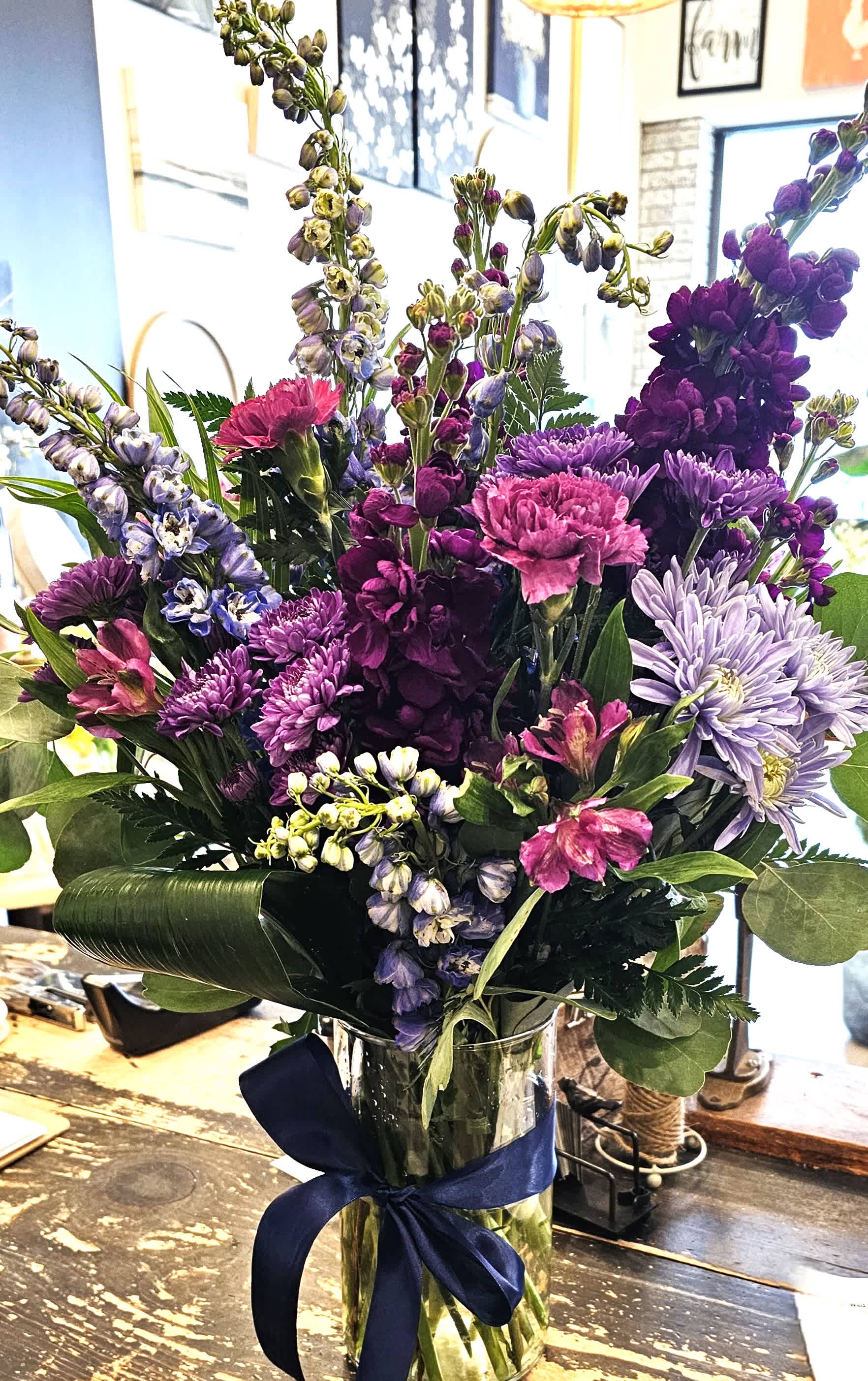 Purple and pink mixed bouquet in a glass vase with a navy ribbon