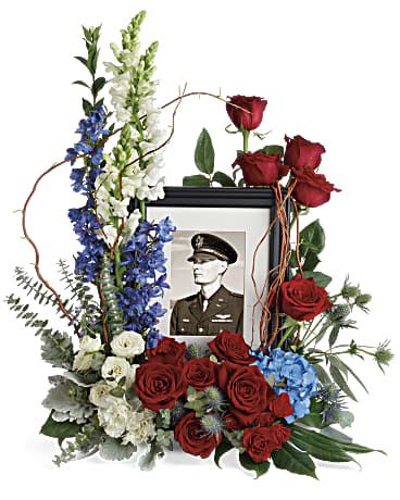 Floral tribute around a framed portrait with red roses and blue and white flowers