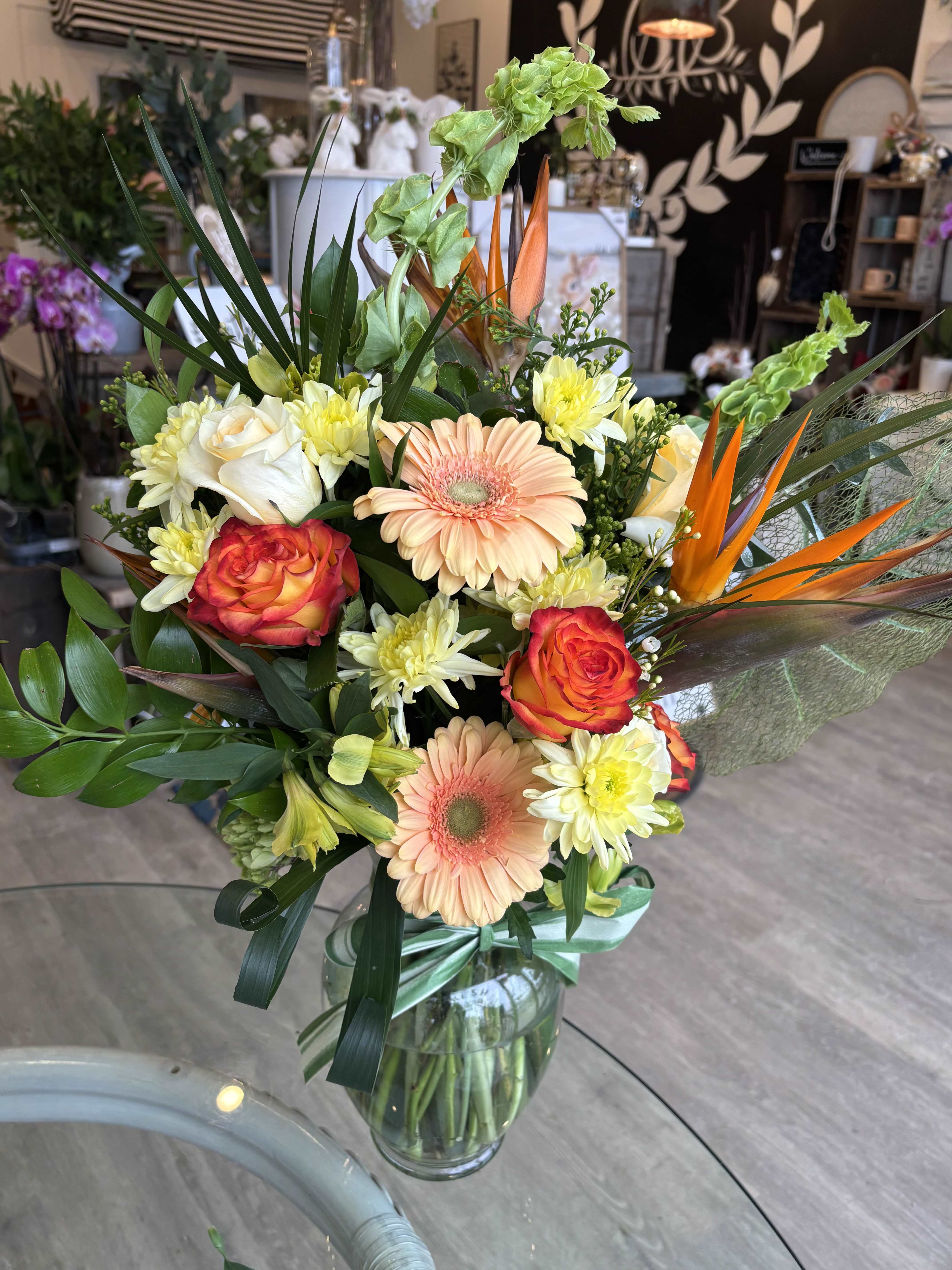 Mixed bouquet with peach gerberas, orange roses, and white daisies in a glass vase