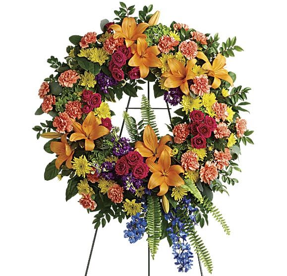 Colorful floral wreath on a black easel with orange lilies and mixed blooms