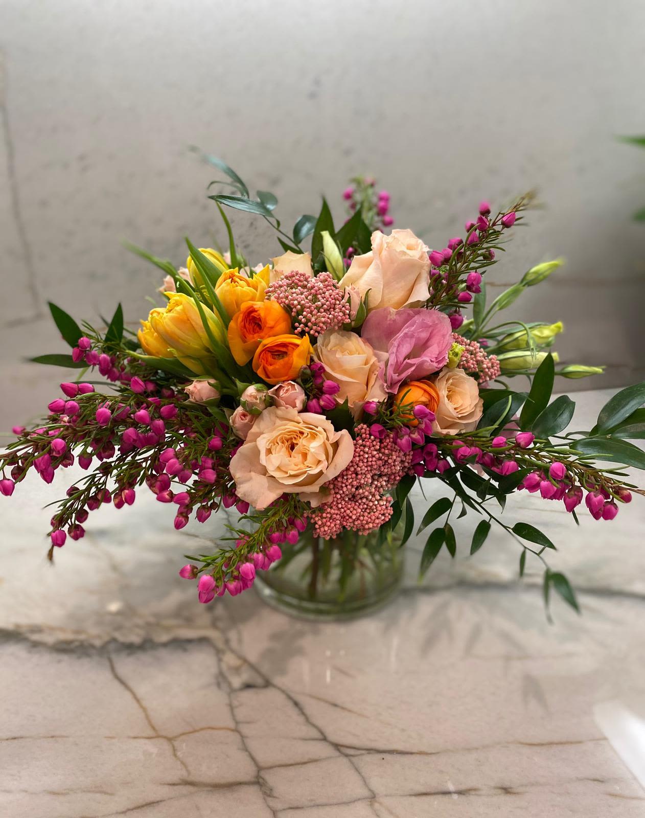 Mixed bouquet of peach, pink, and yellow flowers in a glass vase