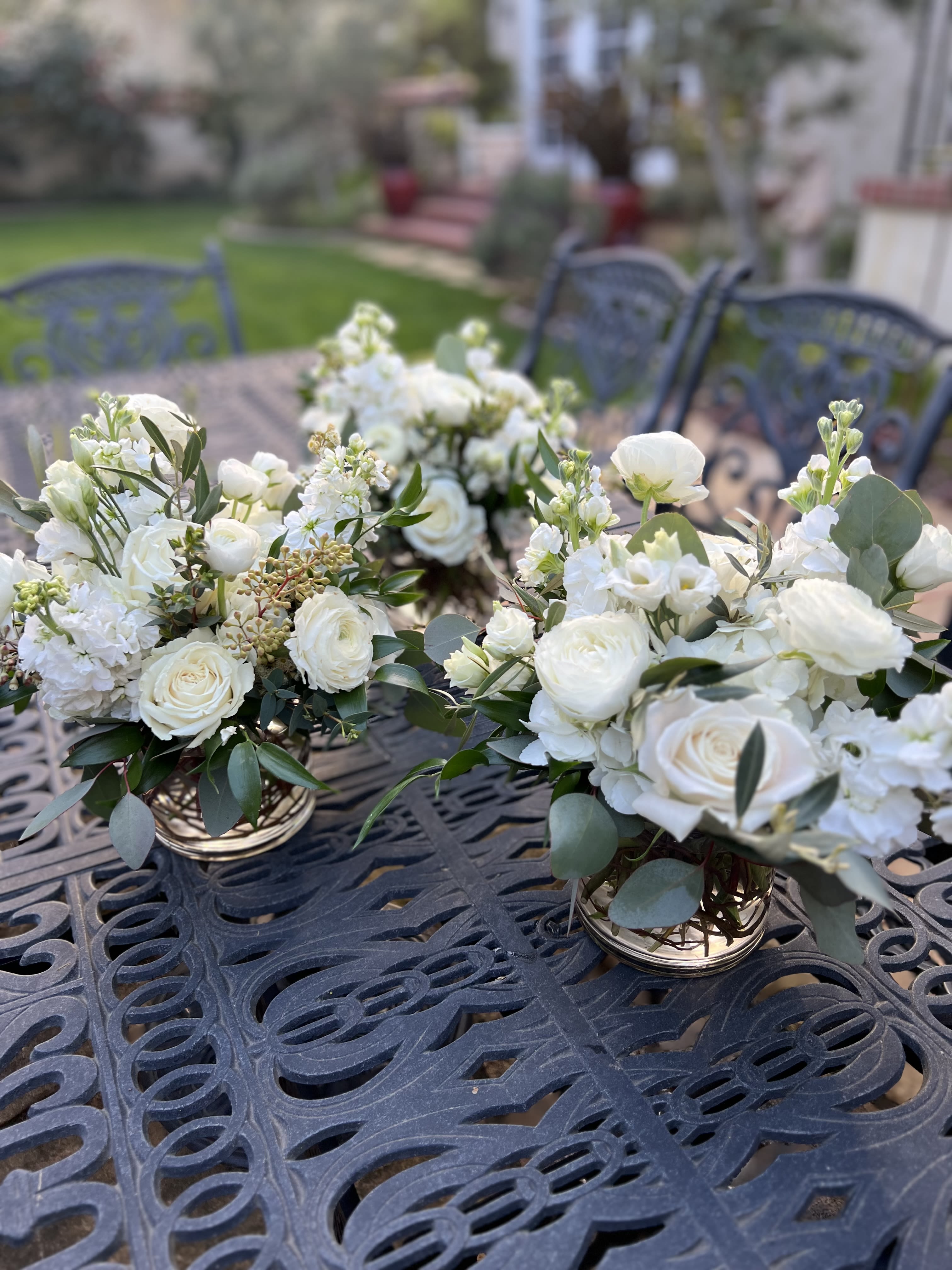White floral centerpieces in low gold containers on an outdoor table